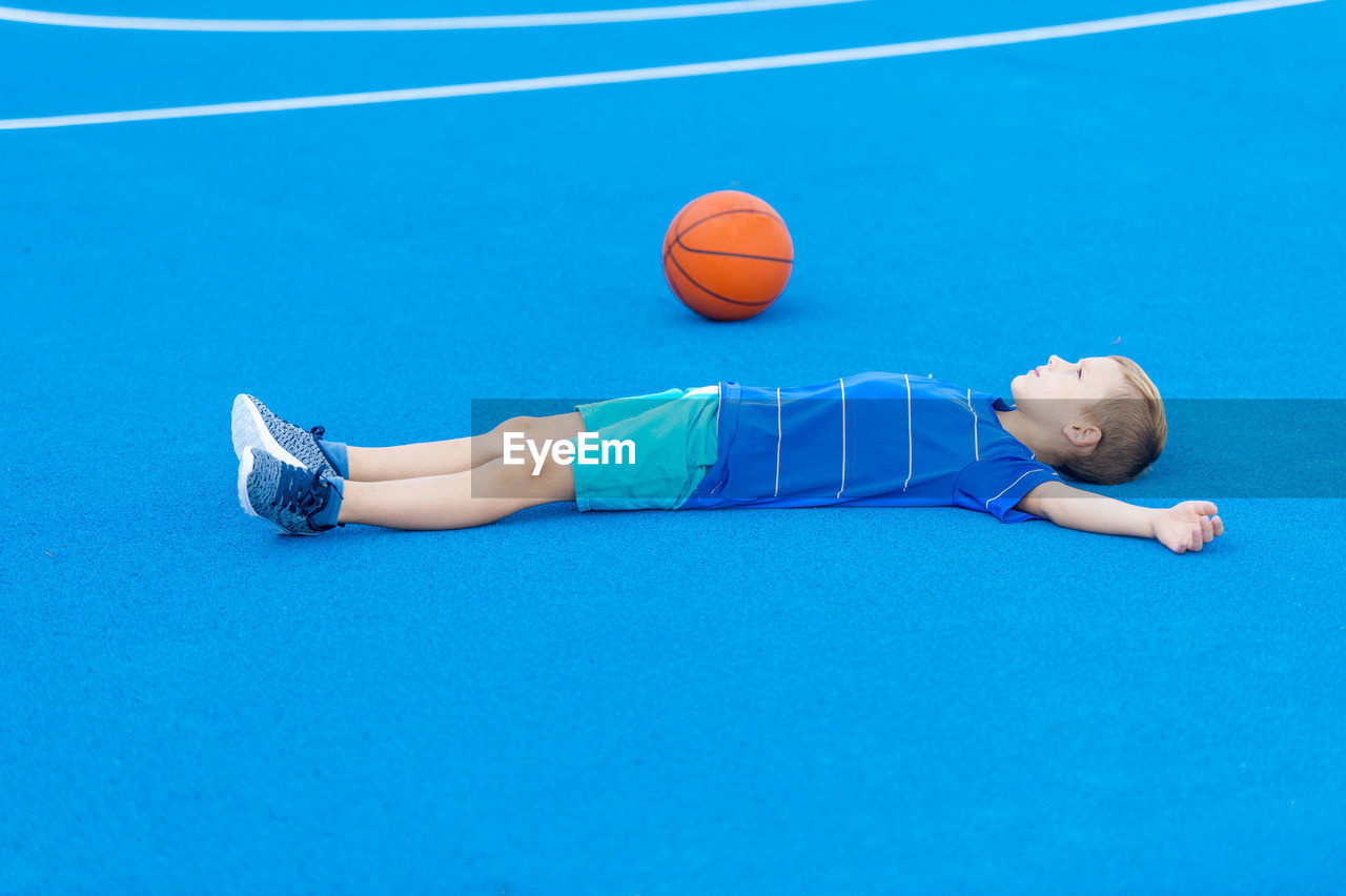 Boy lying by basketball on sports court