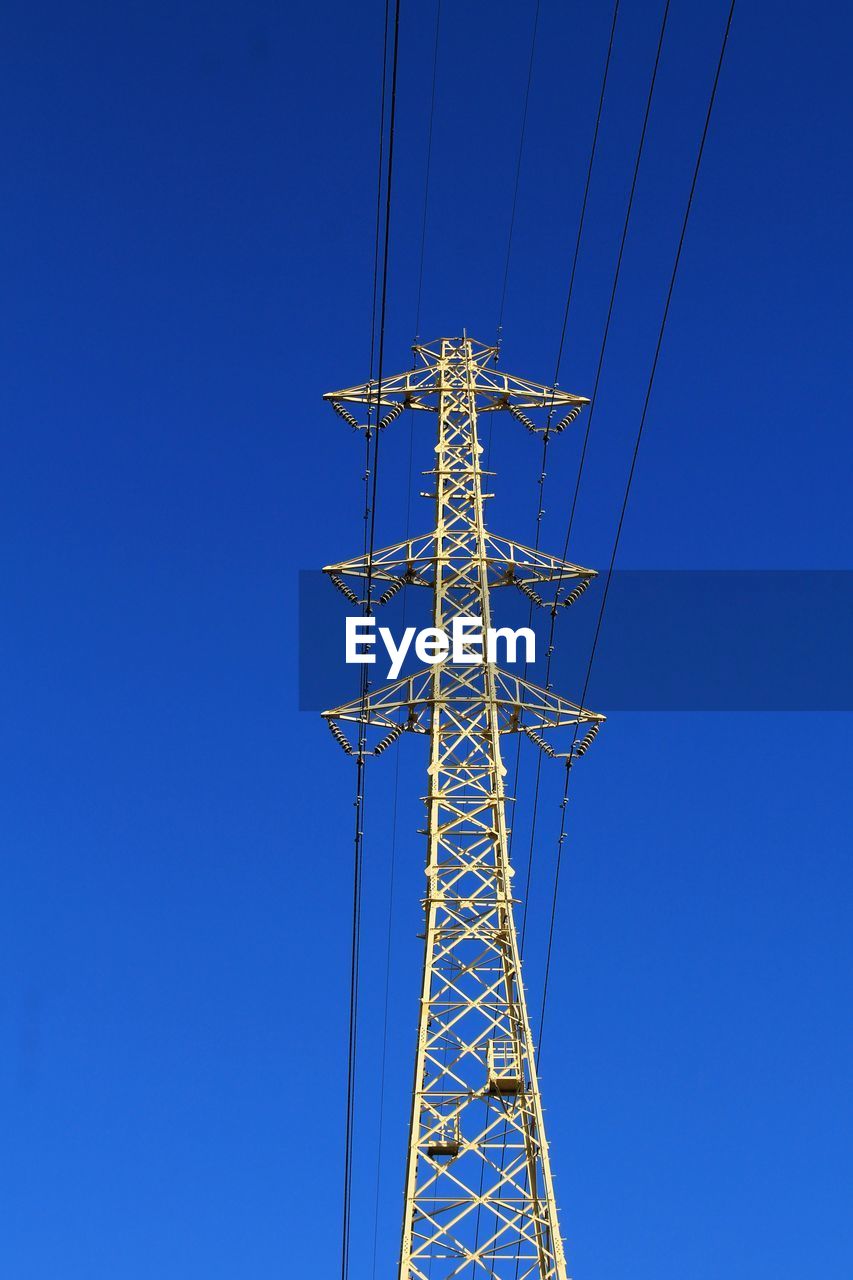 Low angle view of electricity pylon against clear blue sky