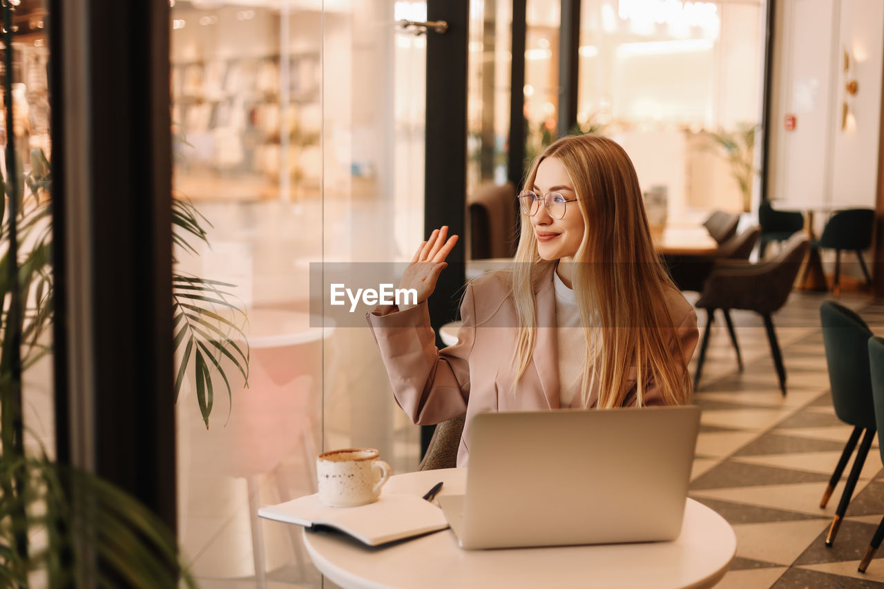 Portrait of a young business woman in glasses and business clothes looking at the camera in a cafe