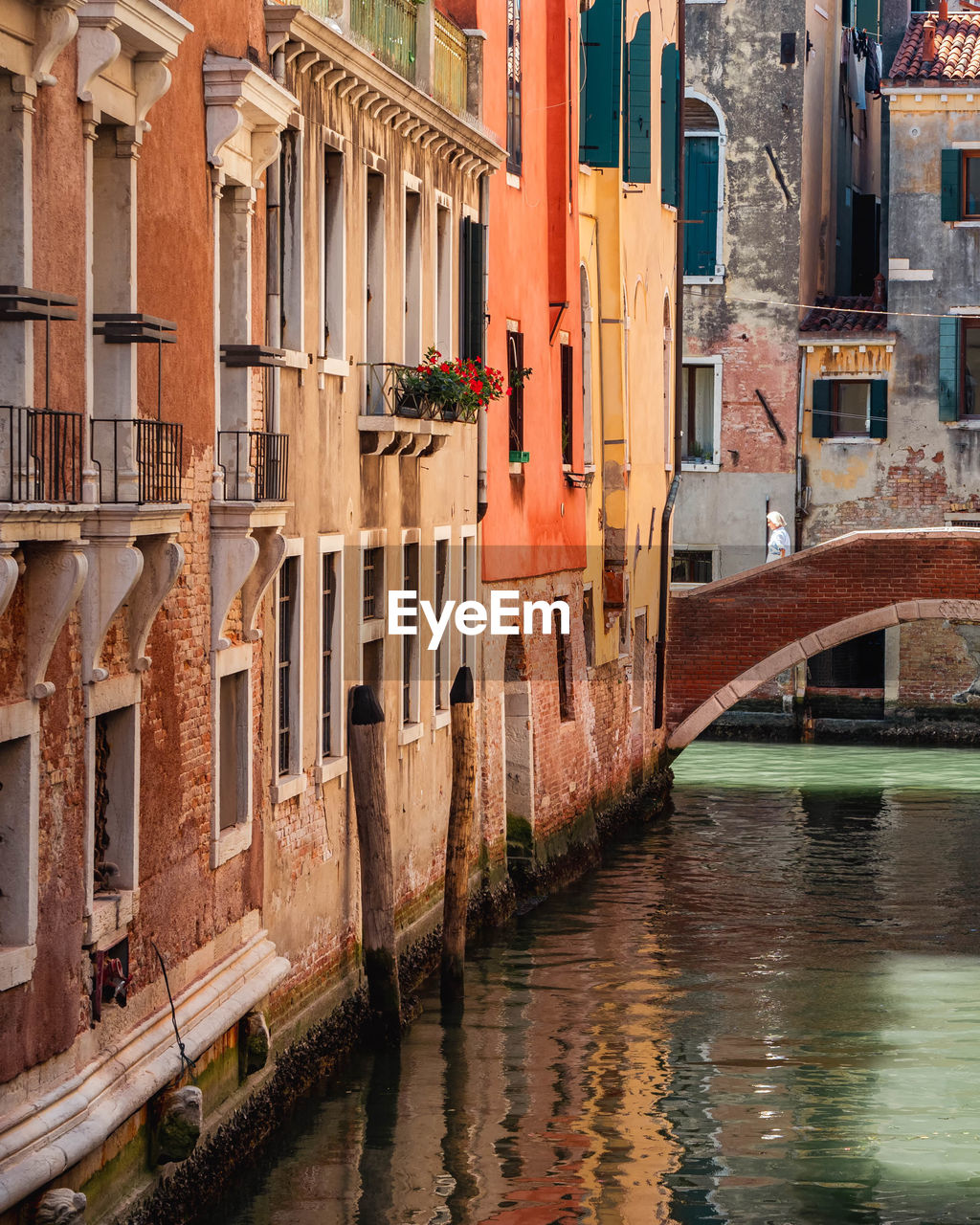 Colorful buildings and a woman walking across a bridge over a canal in venice, italy