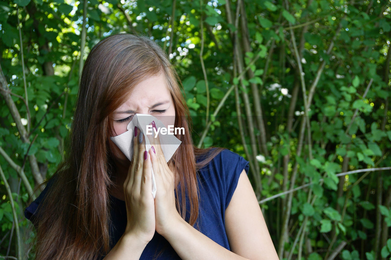 Sick woman wiping her nose against plants