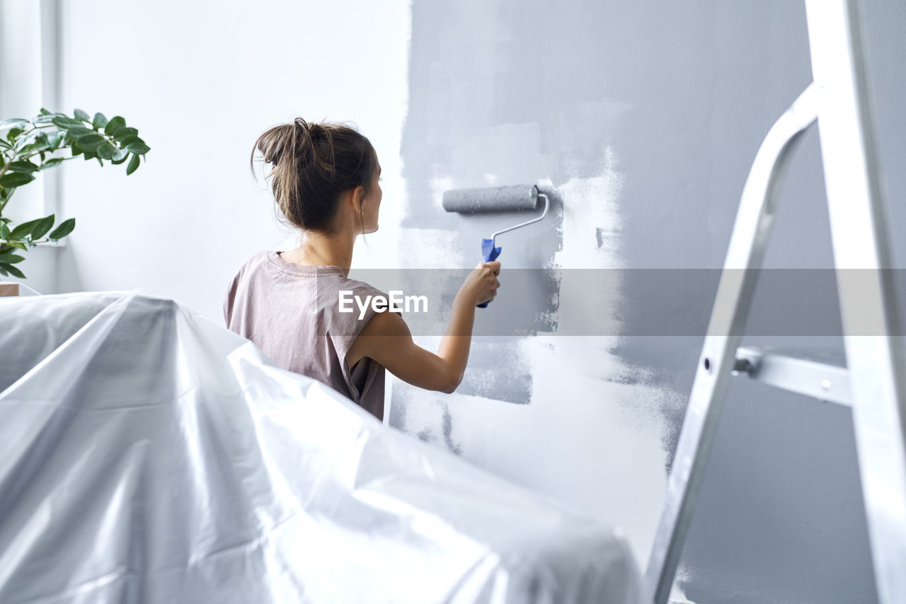 Young woman using paint roller while painting wall at home