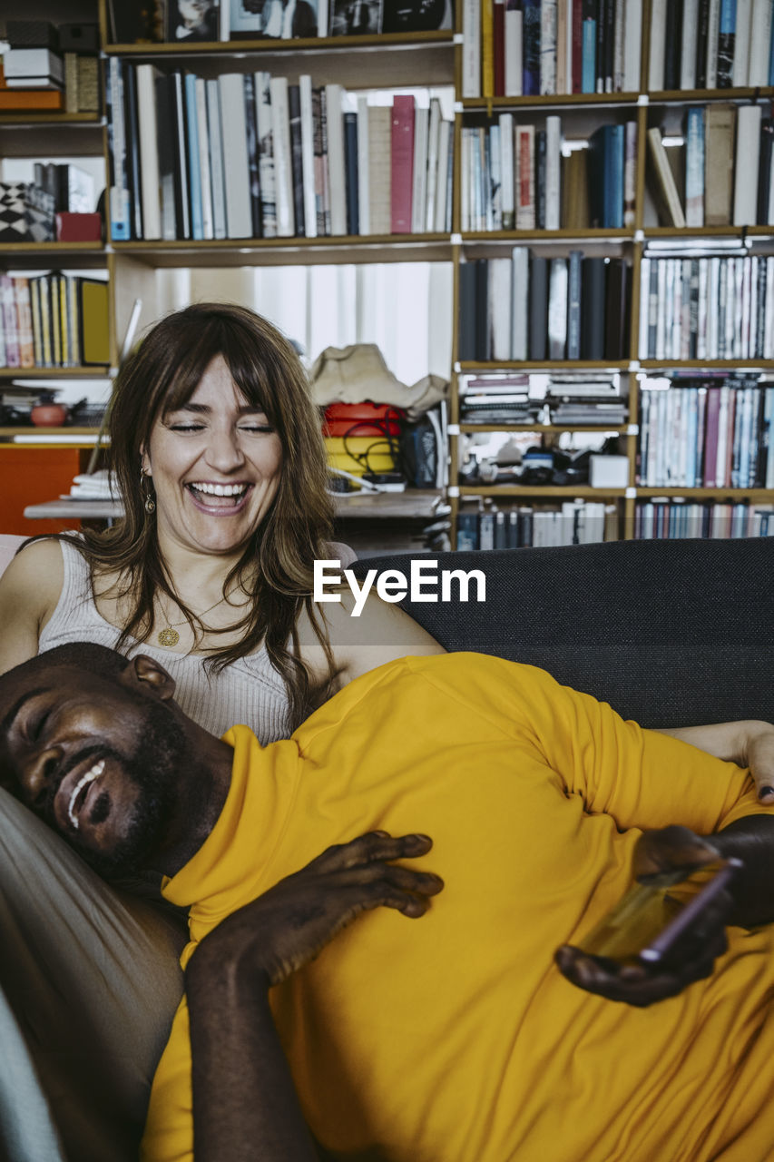 Cheerful man leaning on girlfriend laughing sitting on sofa in living room at home