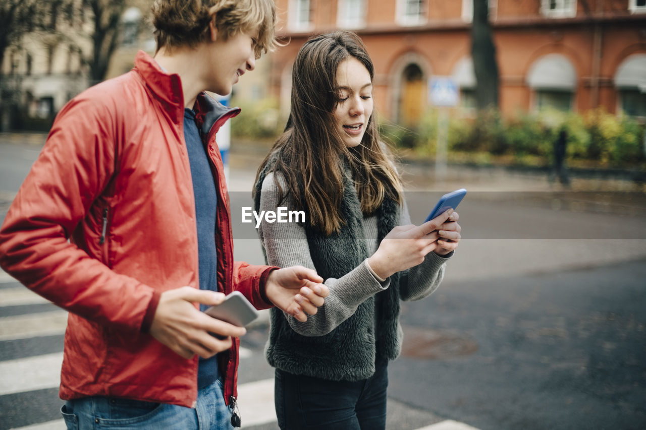 Girl talking while showing mobile phone to male friend on city street