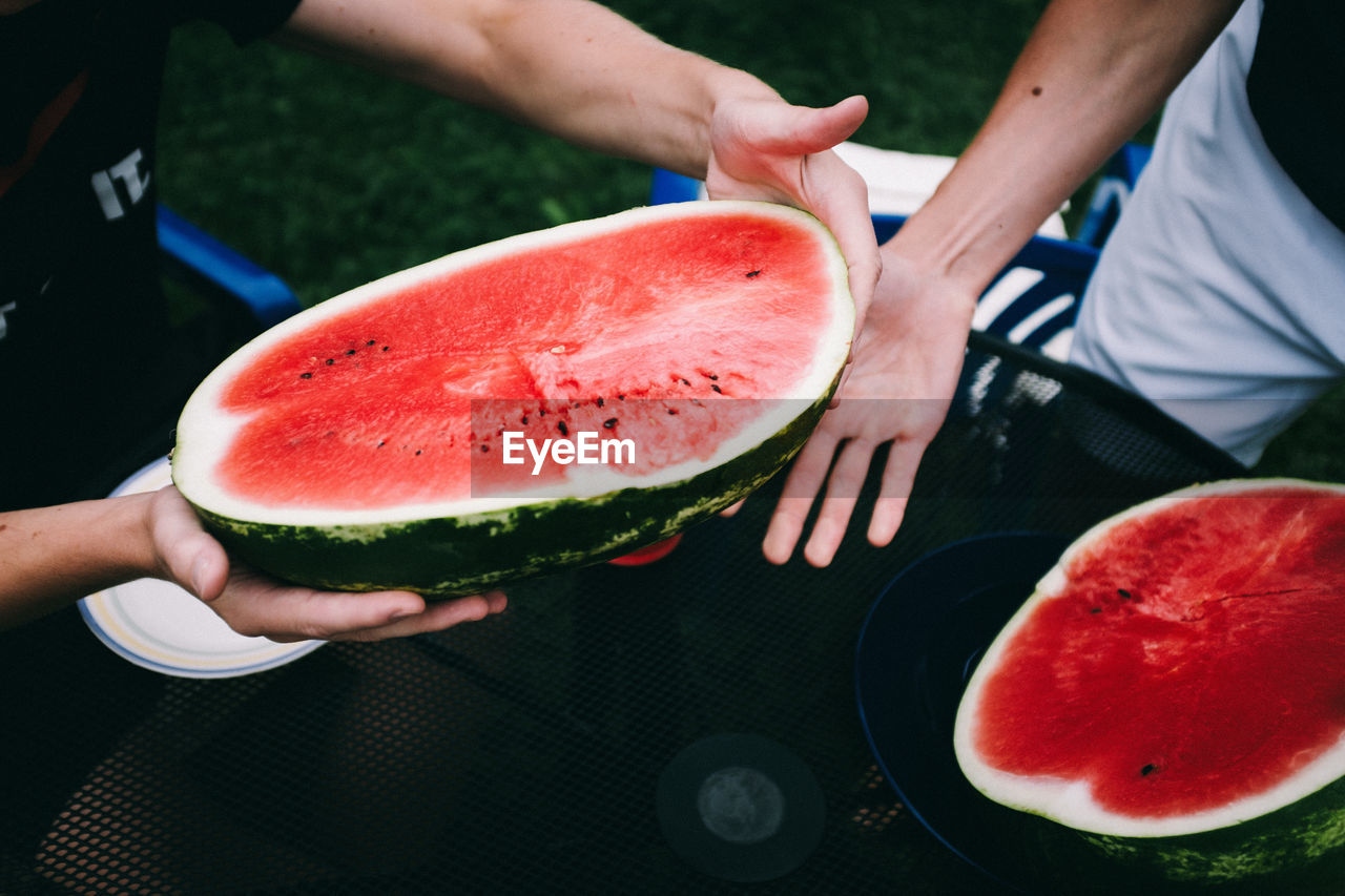 Midsection of people holding watermelon on table