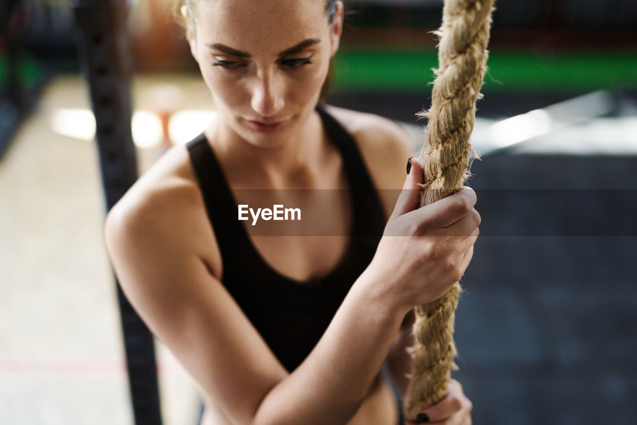 High angle view of young woman holding rope looking away while standing in gym
