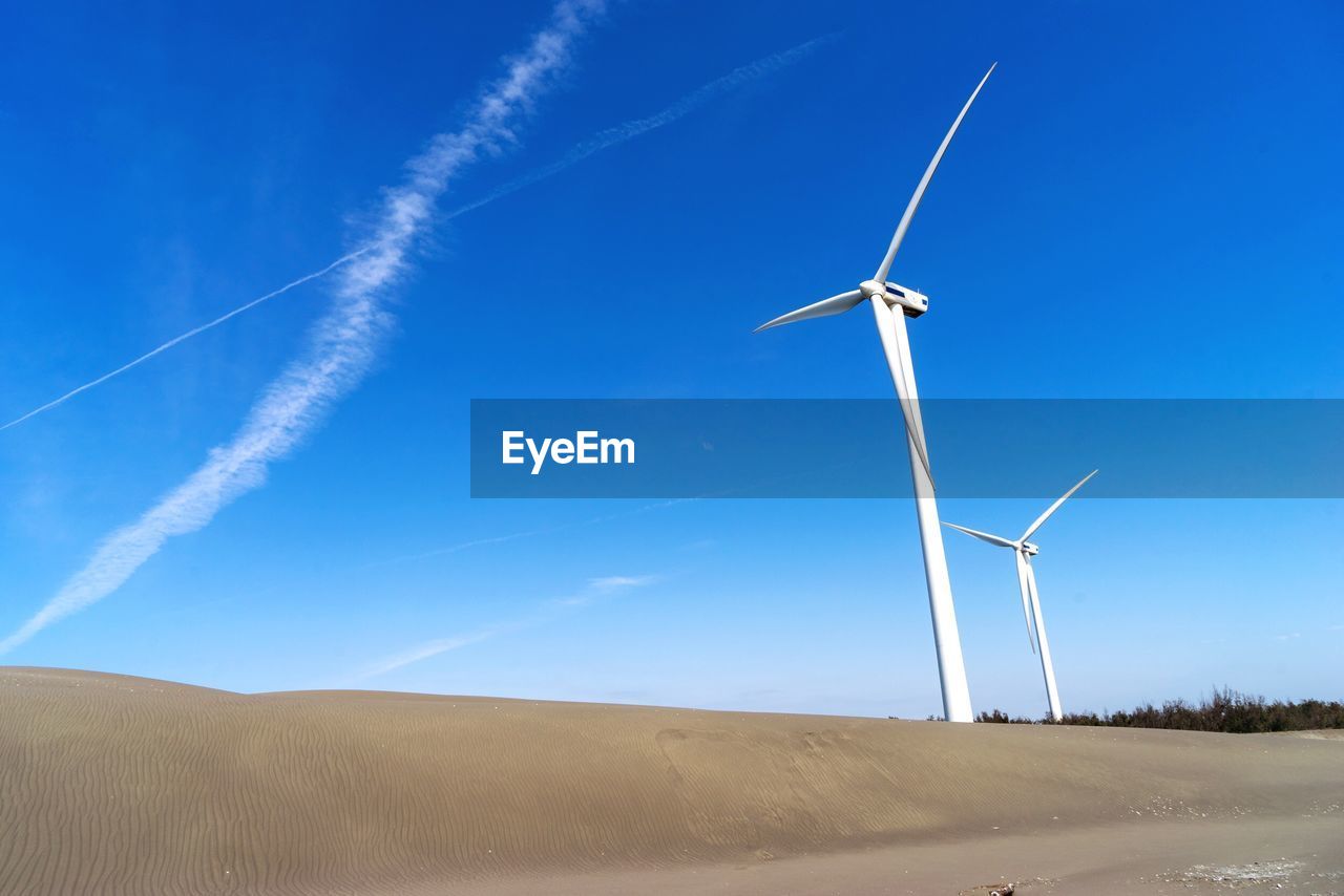 Low angle view of wind turbines on land against blue sky