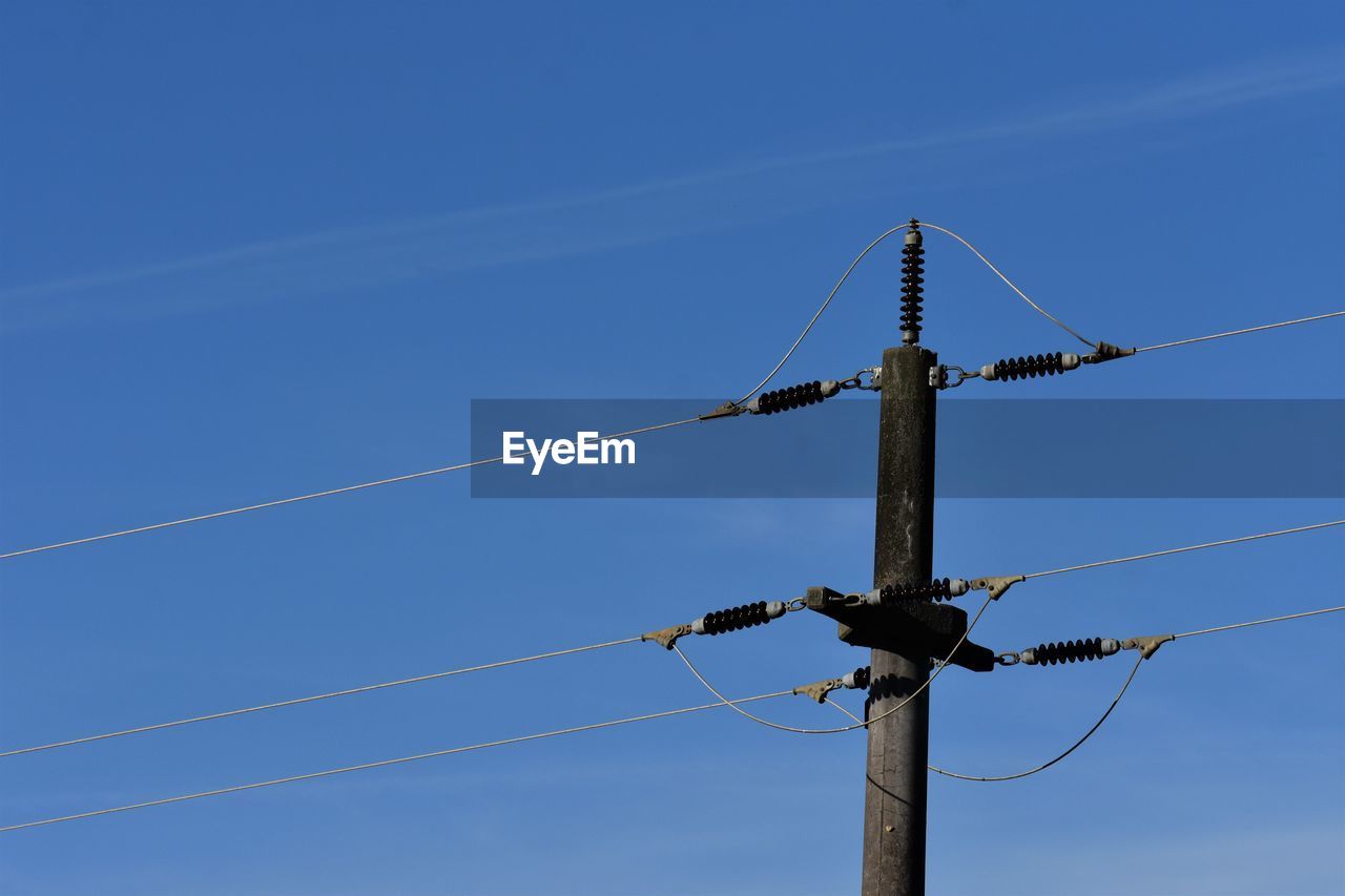 Low angle view of electricity pylon against blue sky