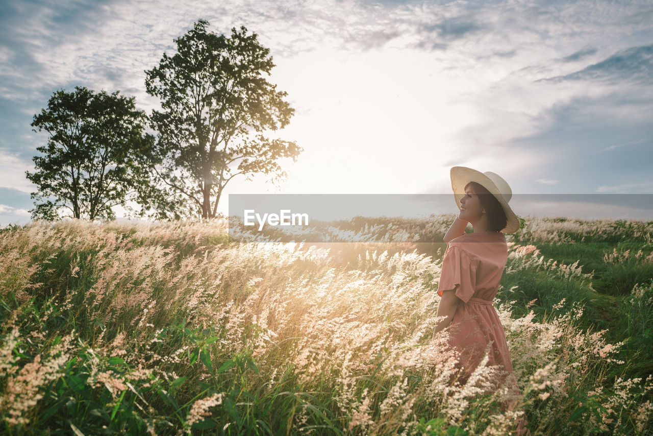 An asian girl on a beautiful spring meadow at sunset. she wears a pink dress and wide-brimmed hat.