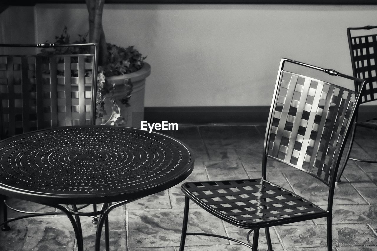 CLOSE-UP OF EMPTY CHAIRS AND TABLE AGAINST WALL