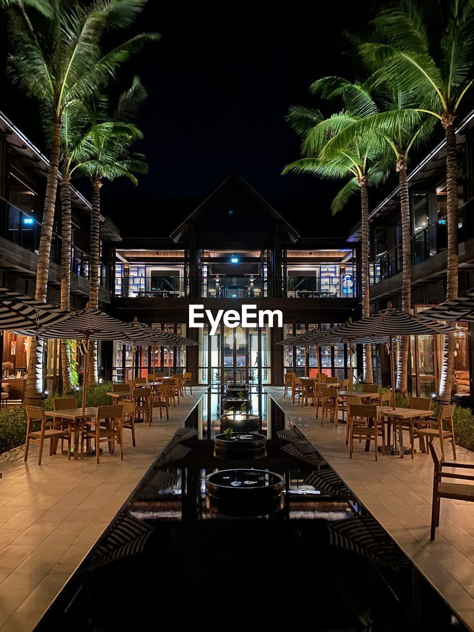 night, architecture, illuminated, built structure, lighting, tropical climate, seat, palm tree, tree, evening, nature, plant, resort, travel destinations, table, building exterior, chair, no people, bar, outdoors, restaurant, building, water, travel, lighting equipment
