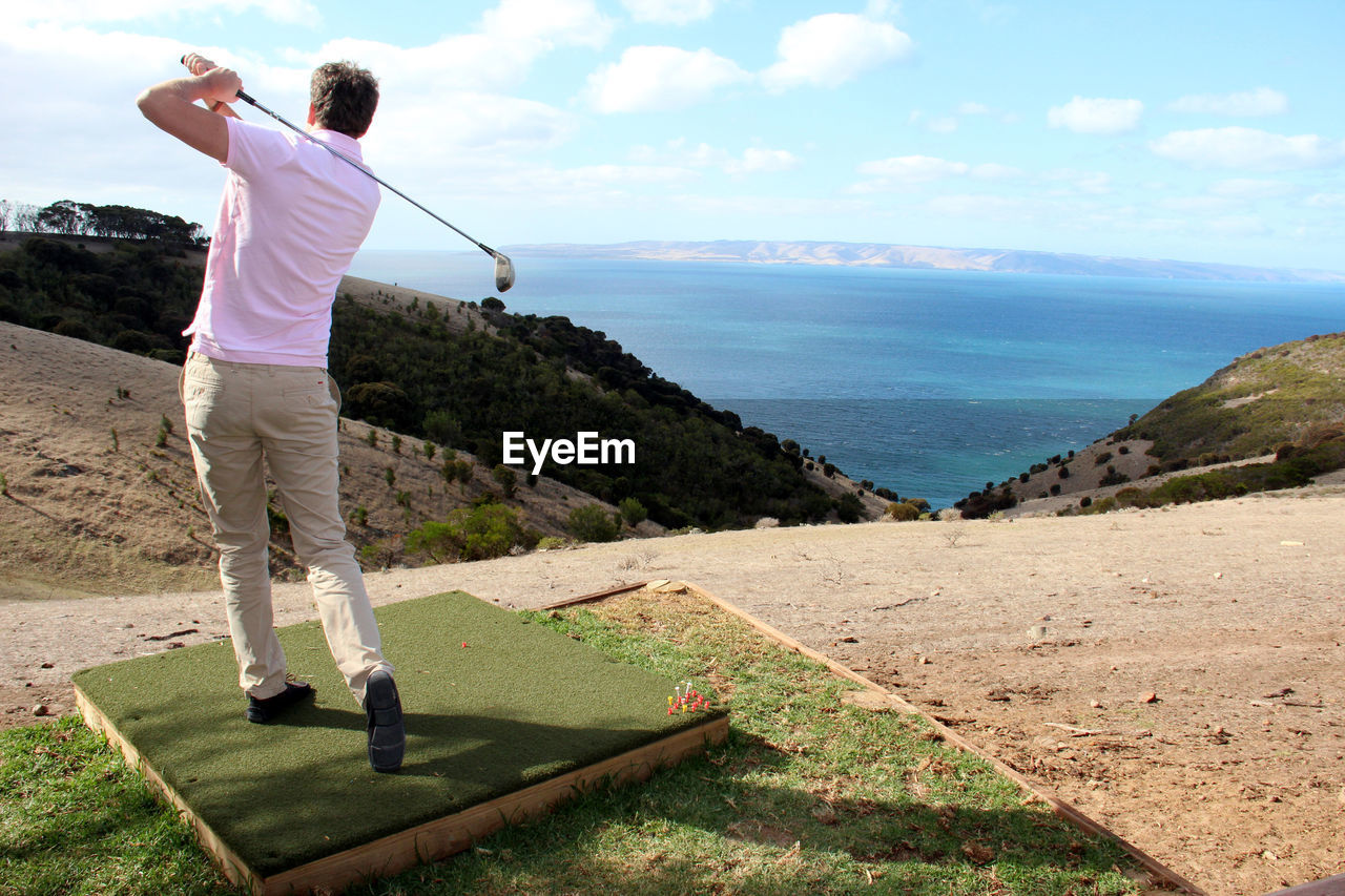 Rear view of man playing golf against sea