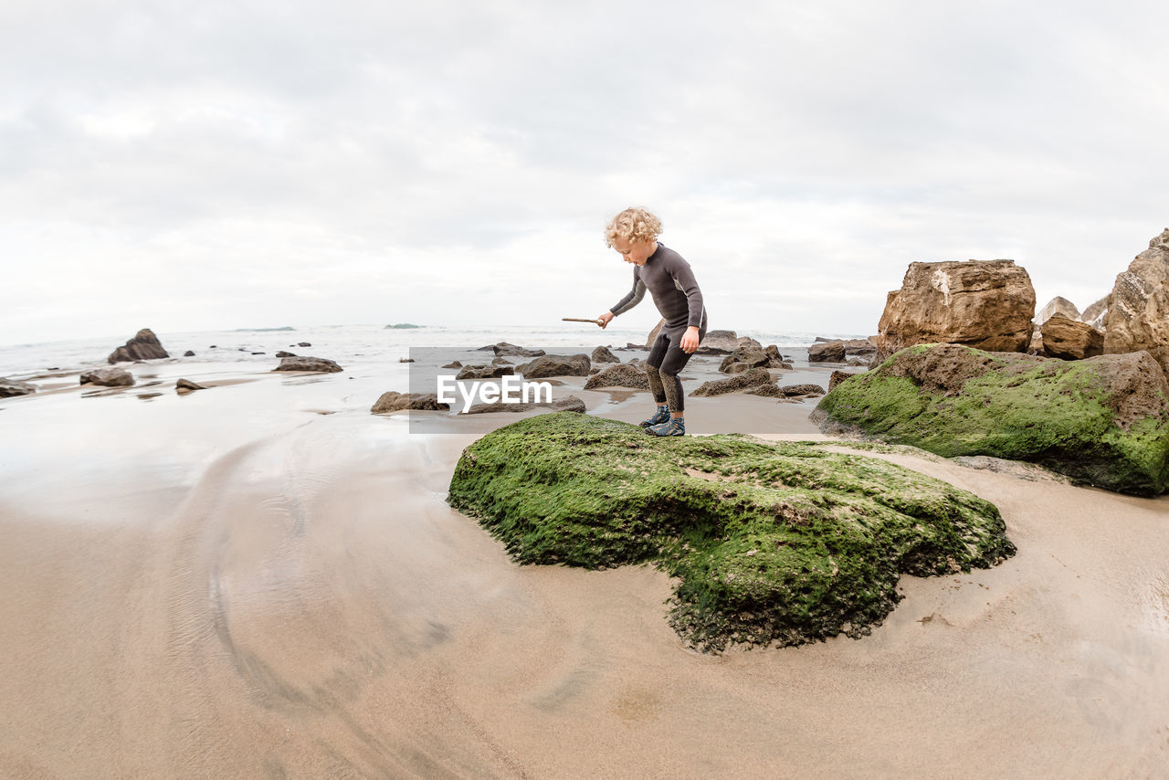 Toddler boy standing on green rock at a beach in new zealand