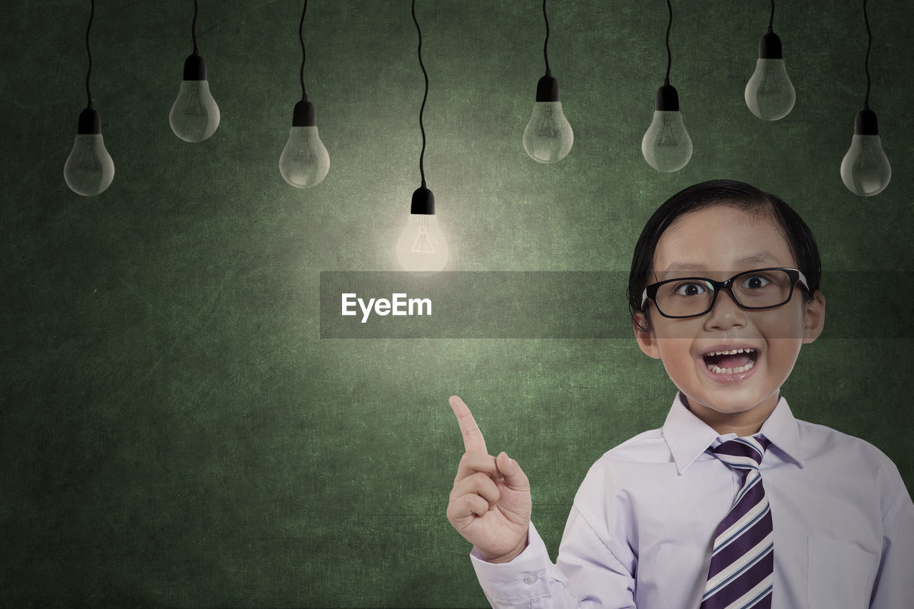 Portrait of boy looking at light bulbs while standing against wall