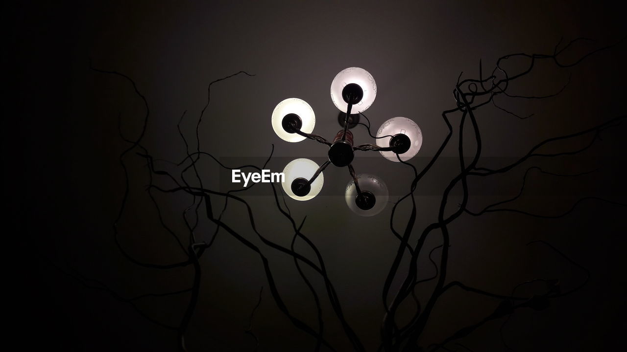 Low angle view of silhouette decor against illuminated chandelier in dark