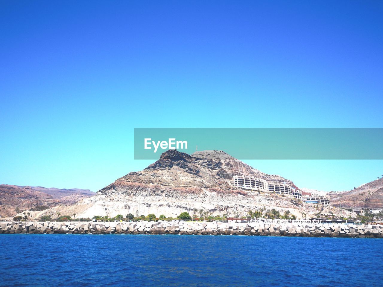 Scenic view of sea and mountains against clear blue sky