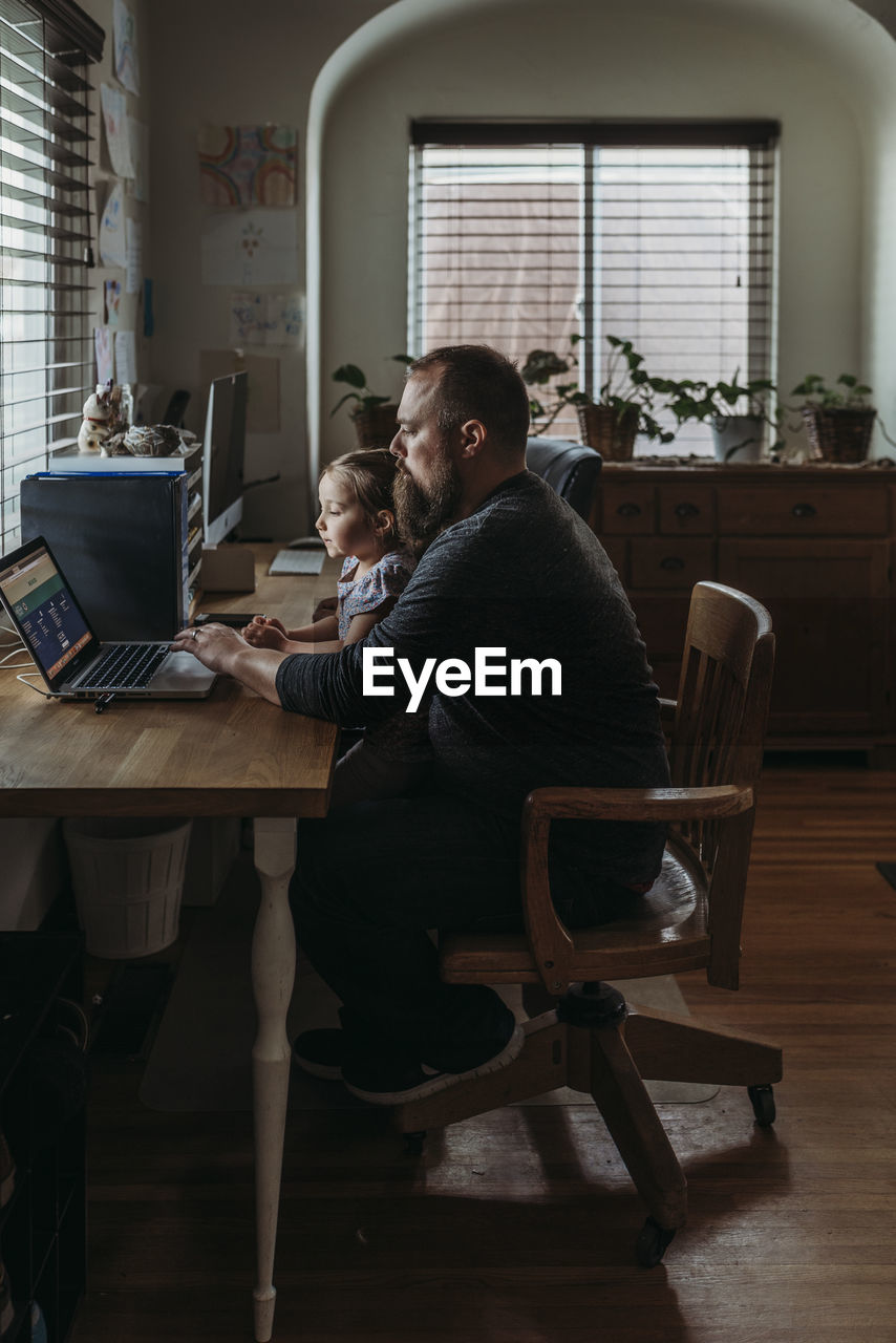 Father with young preschool aged daughter sitting while he works from