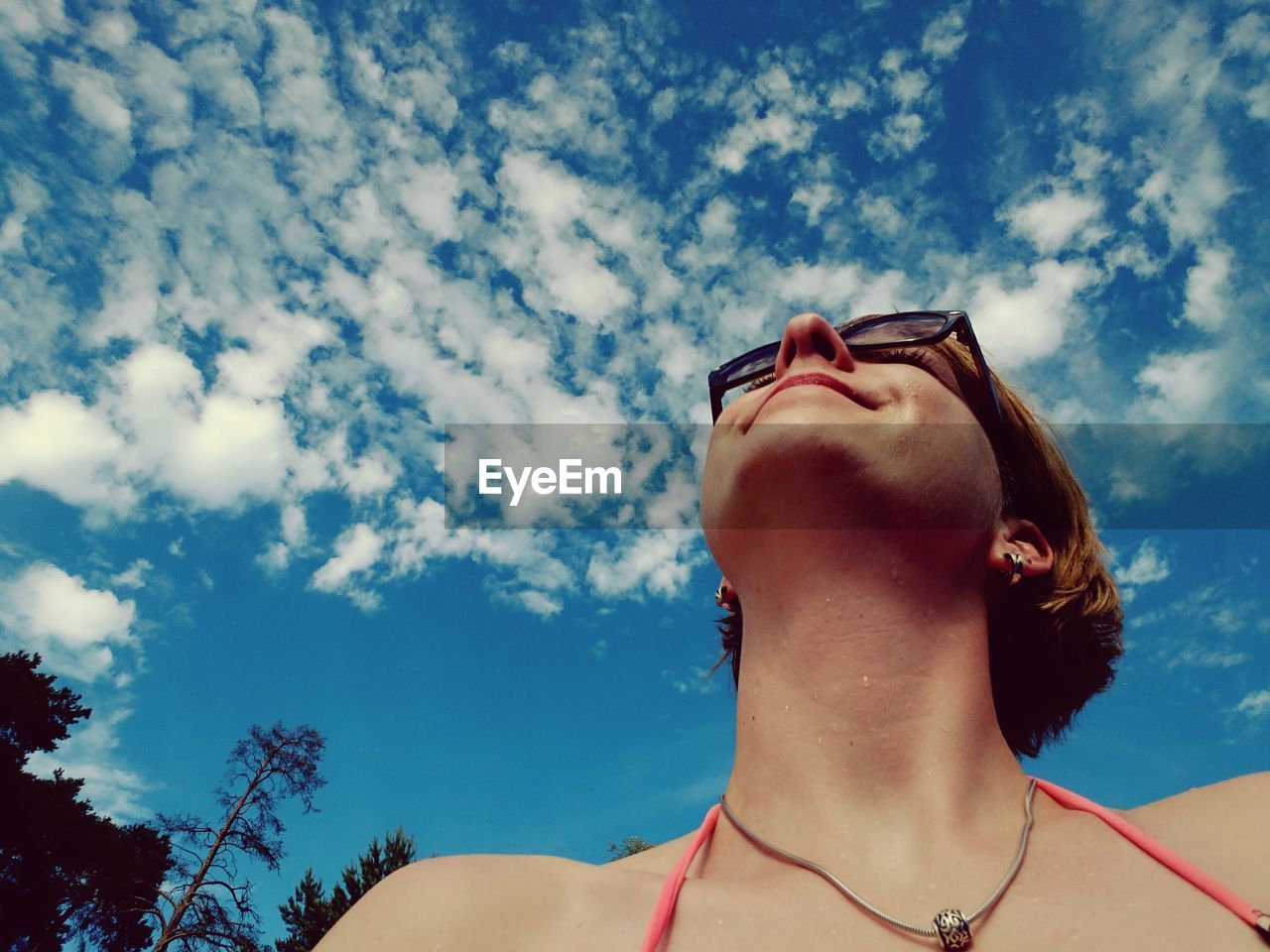 Low angle view of woman wearing eyeglasses looking up against cloudy sky