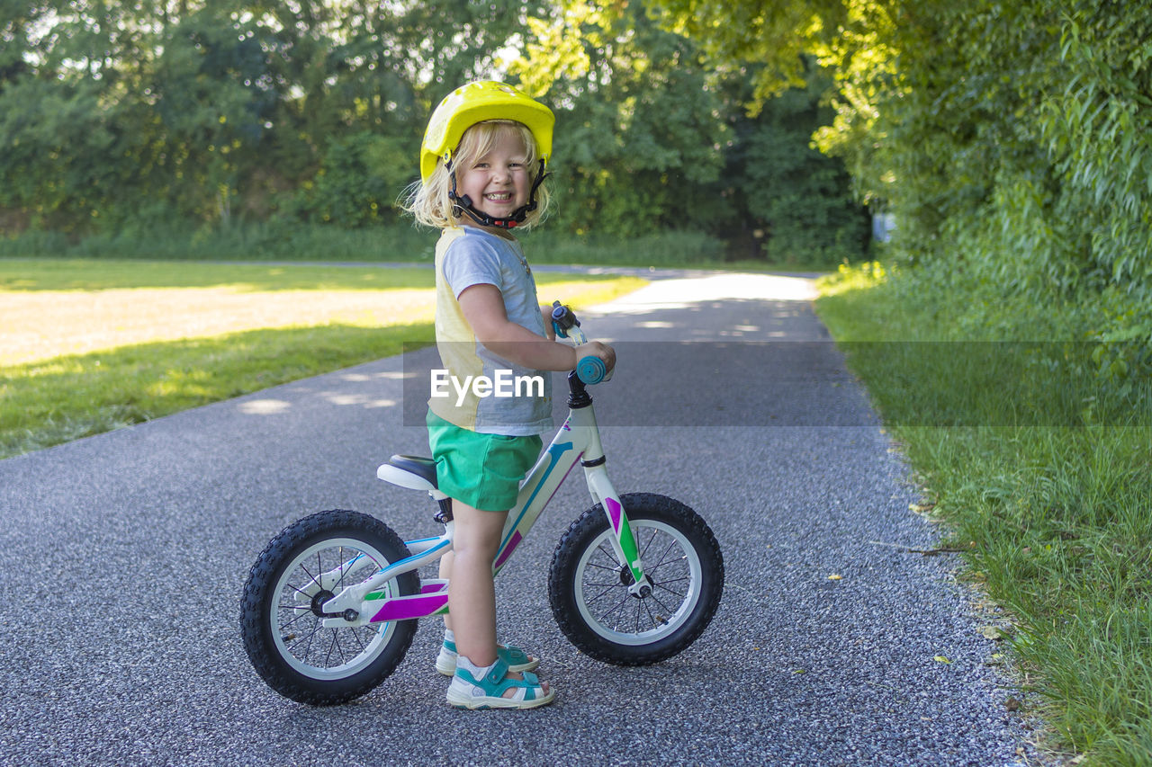 Full length portrait of cute boy with bicycle standing on road