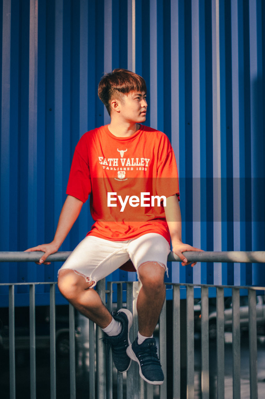 FULL LENGTH OF BOY SITTING ON RAILING AGAINST WALL