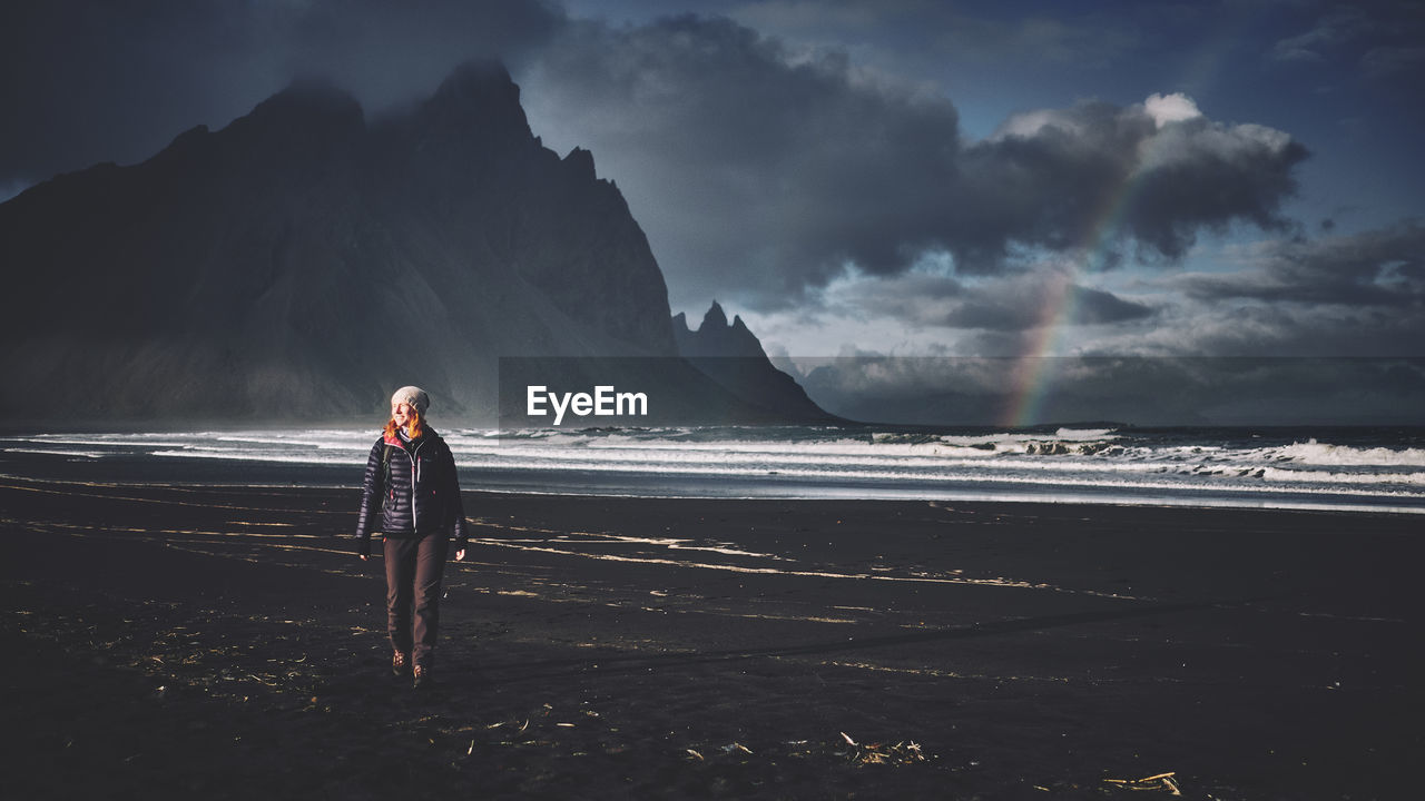 Smiling young woman standing on beach against sky