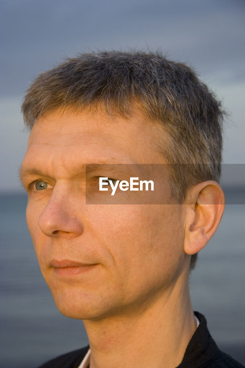 Close-up of mature man looking away with sea in background