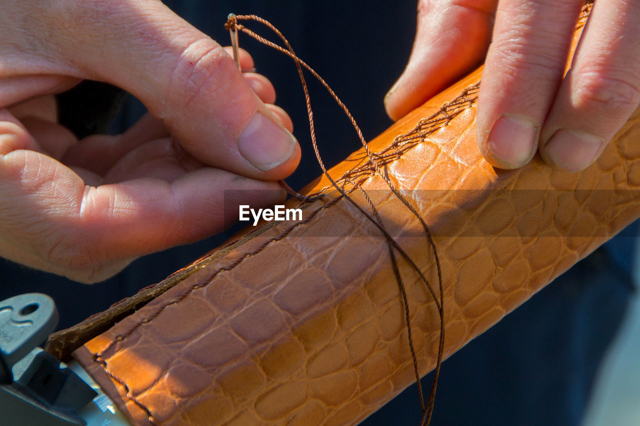 Cropped hands of man stitching leather on metal