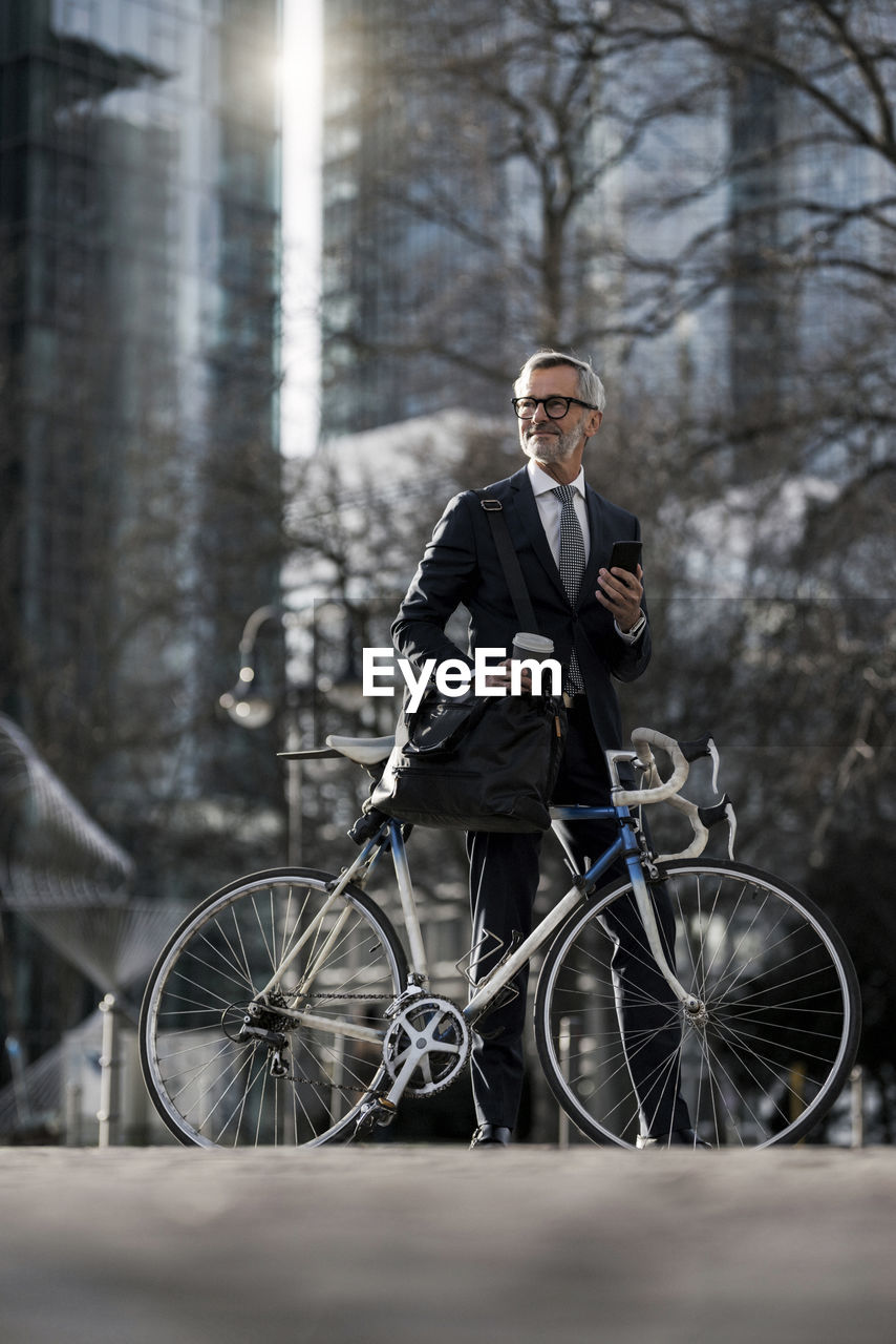 Grey-haired businessman with bicycle and coffee to go in the city