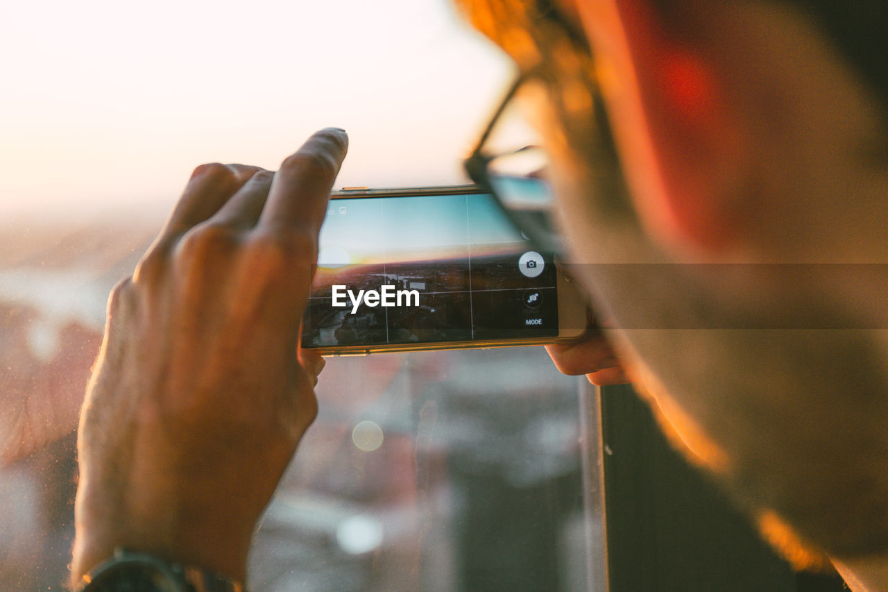 Close-up of man using mobile phone against sunset sky