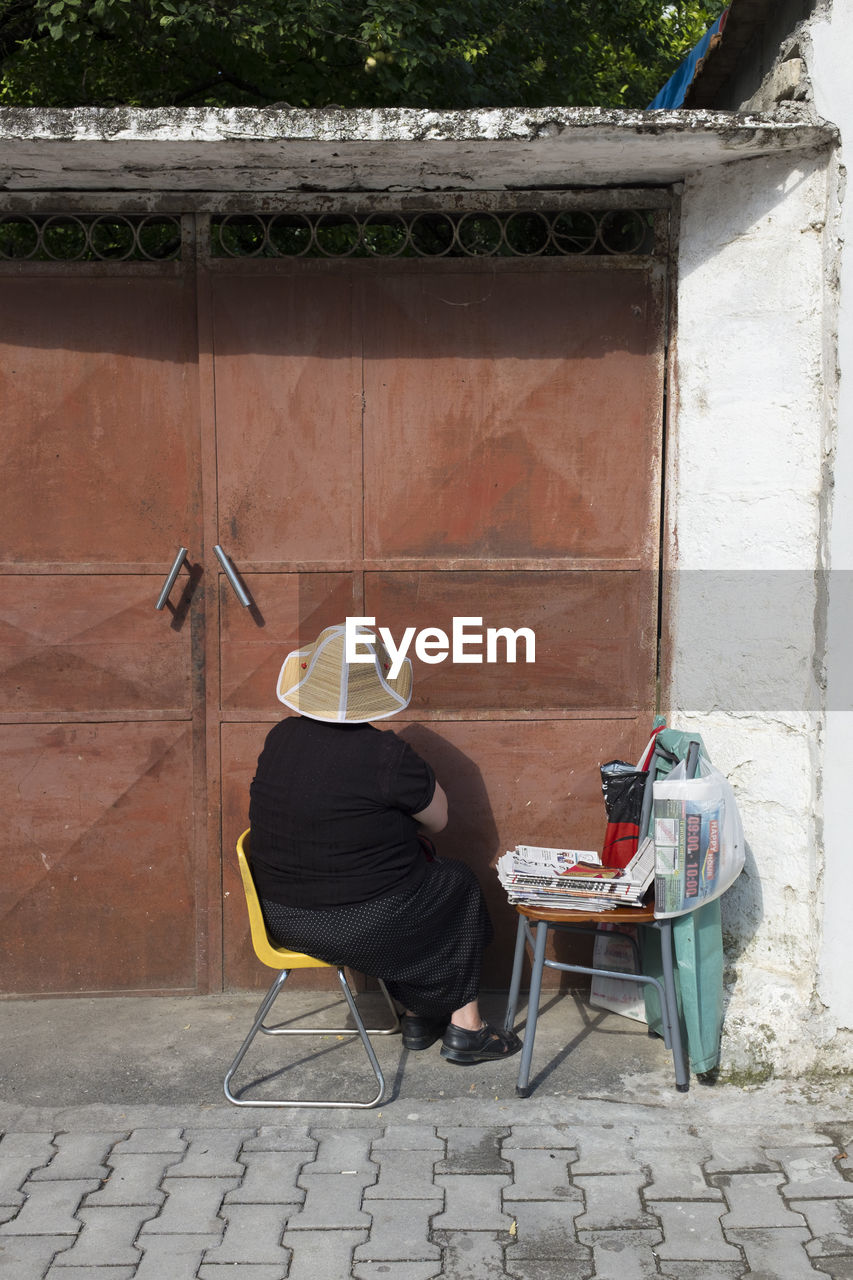 REAR VIEW OF MAN SITTING ON CHAIR IN FOOTPATH