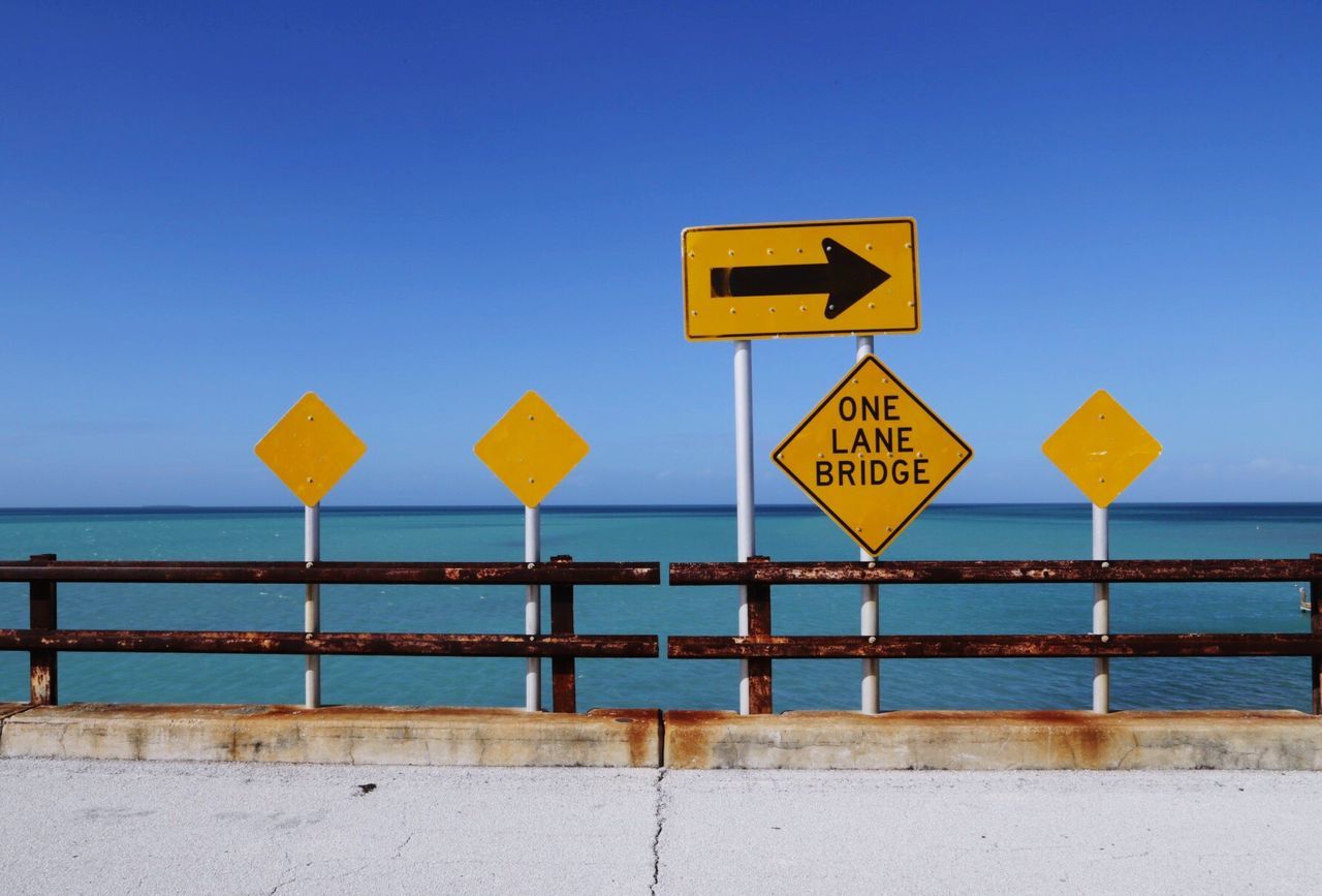 Road sign by sea against clear blue sky