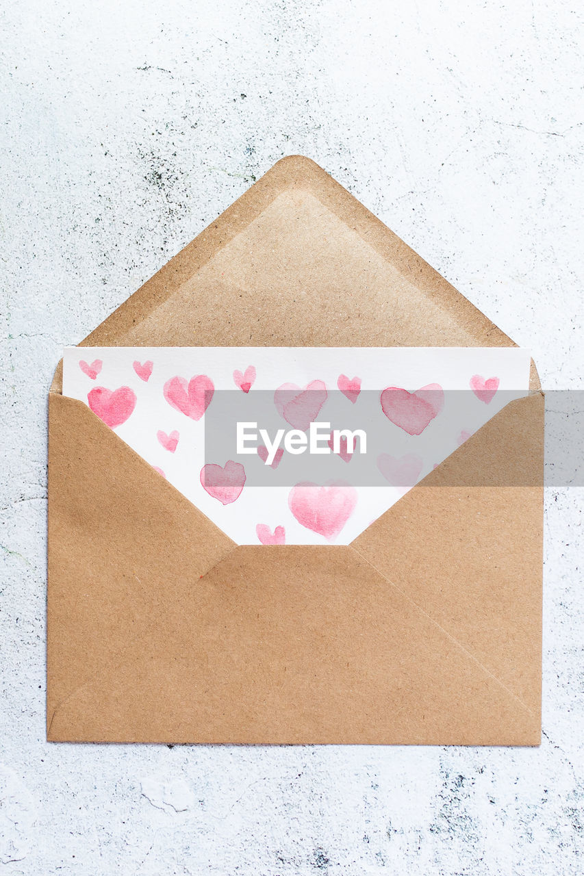 Love letter with water color pink hearts in a craft envelope on white wood background.