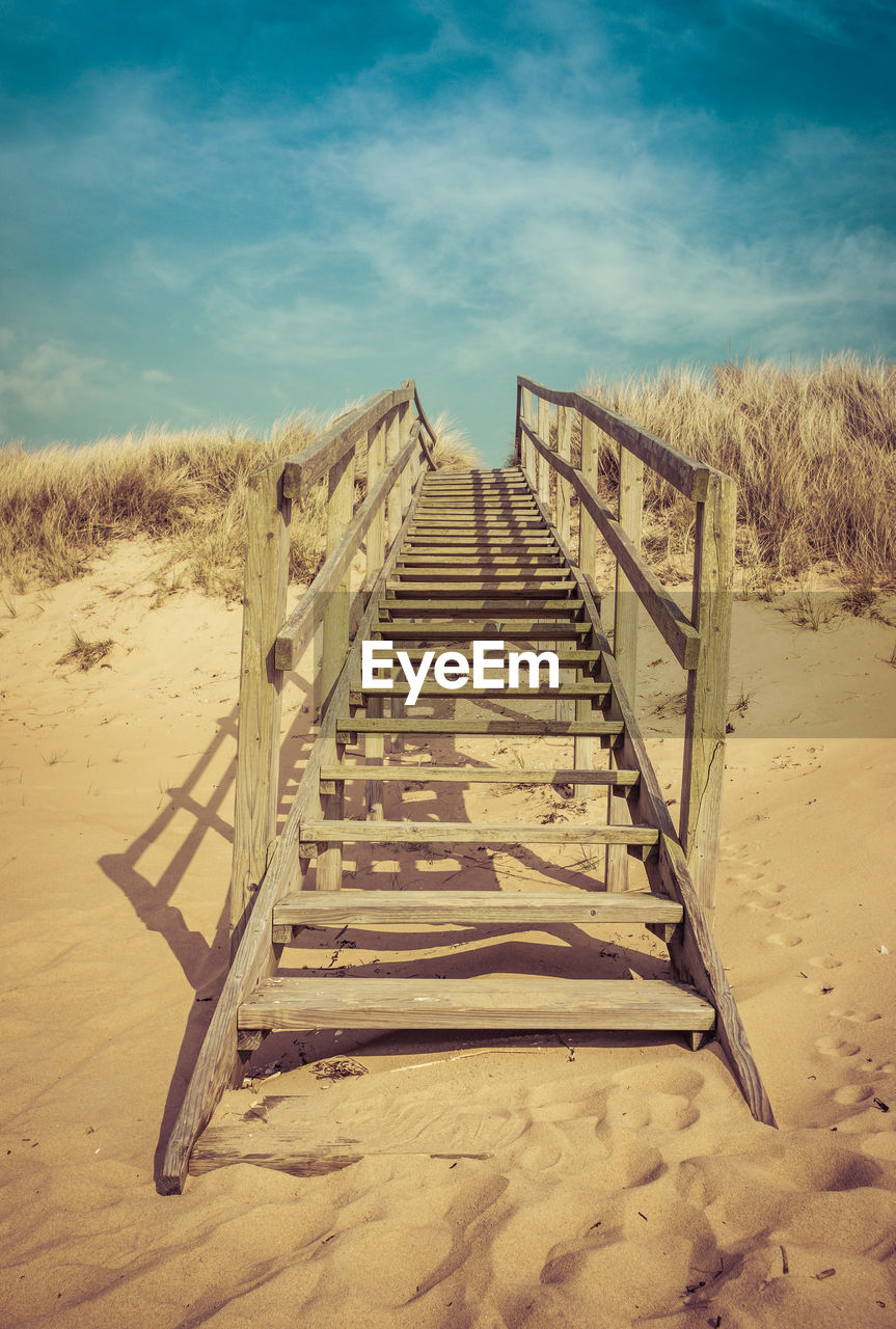 Surface level of boardwalk on beach against sky