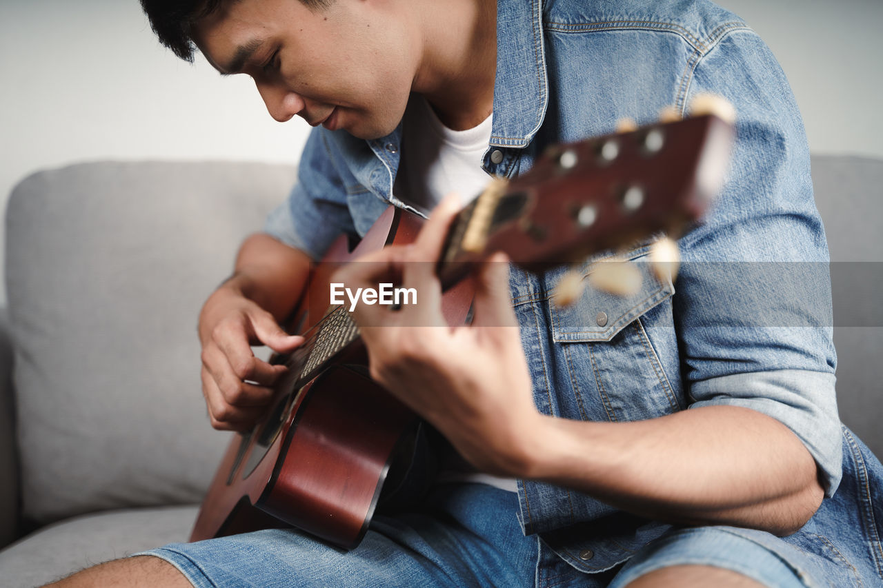 MIDSECTION OF MAN PLAYING GUITAR AT CAMERA
