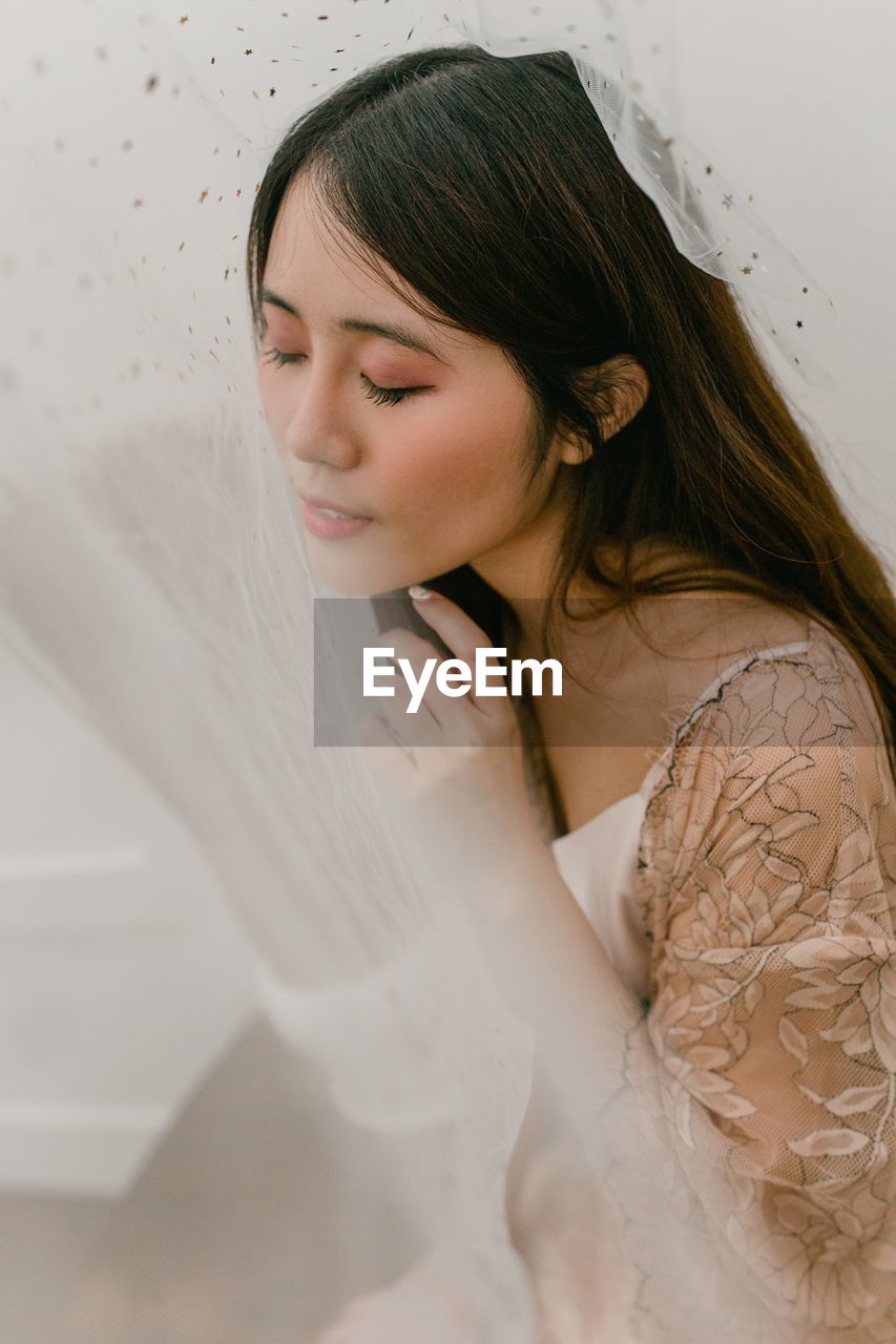 WOMAN LOOKING AWAY WHILE STANDING ON WHITE CURTAIN