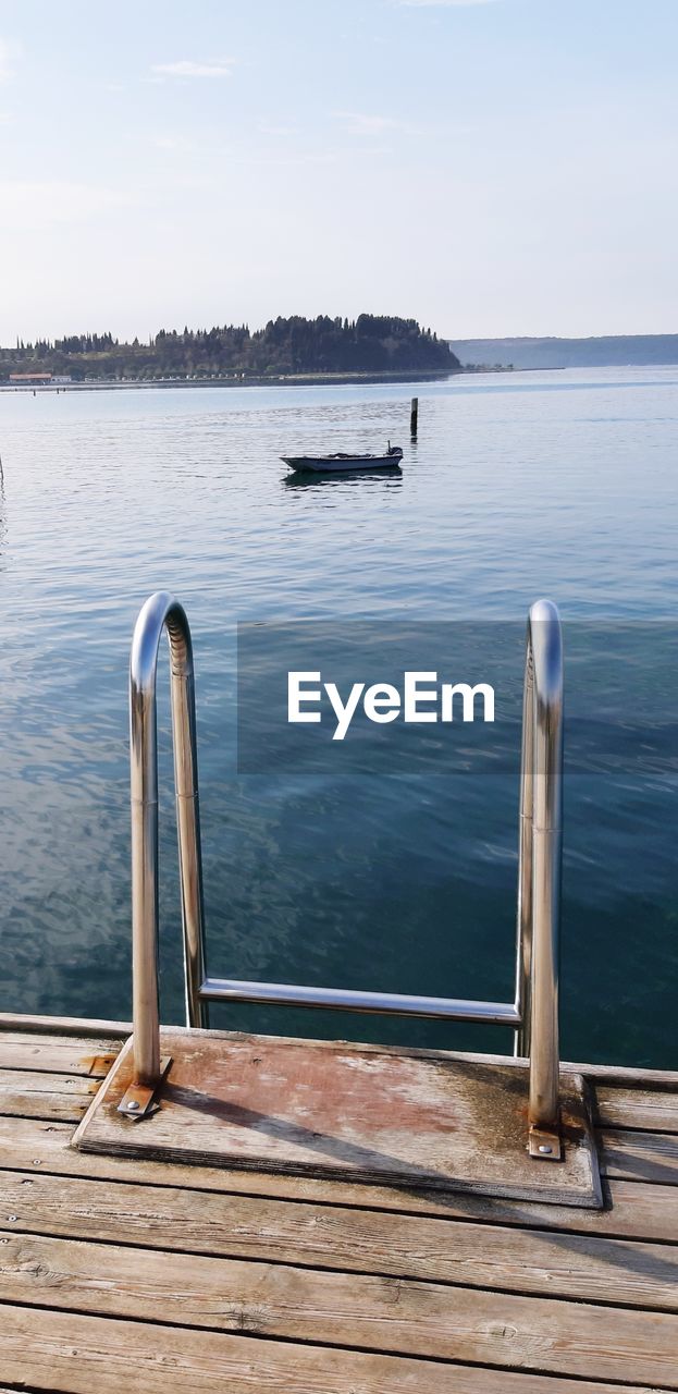 Jetty in swimming pool by lake against sky