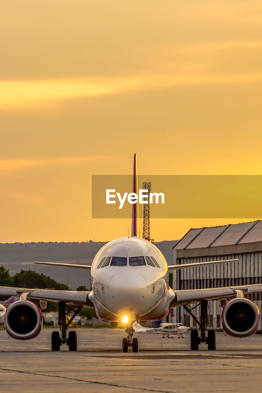 Airplane on airport runway against sky during sunset