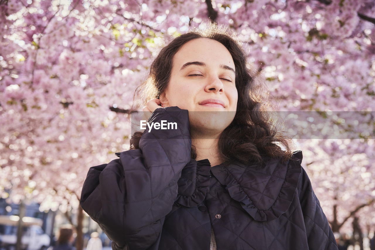 Young woman standing under cherry blossom