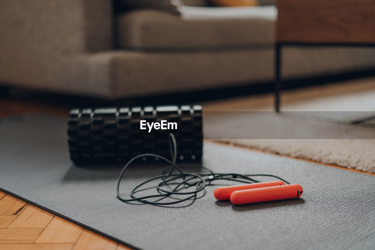 View of a jump rope and a foam roller on a fitness mat, modern interior, selective focus.