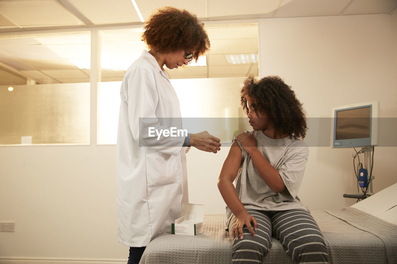 Doctor standing by patient sitting on bed in medical room at hospital