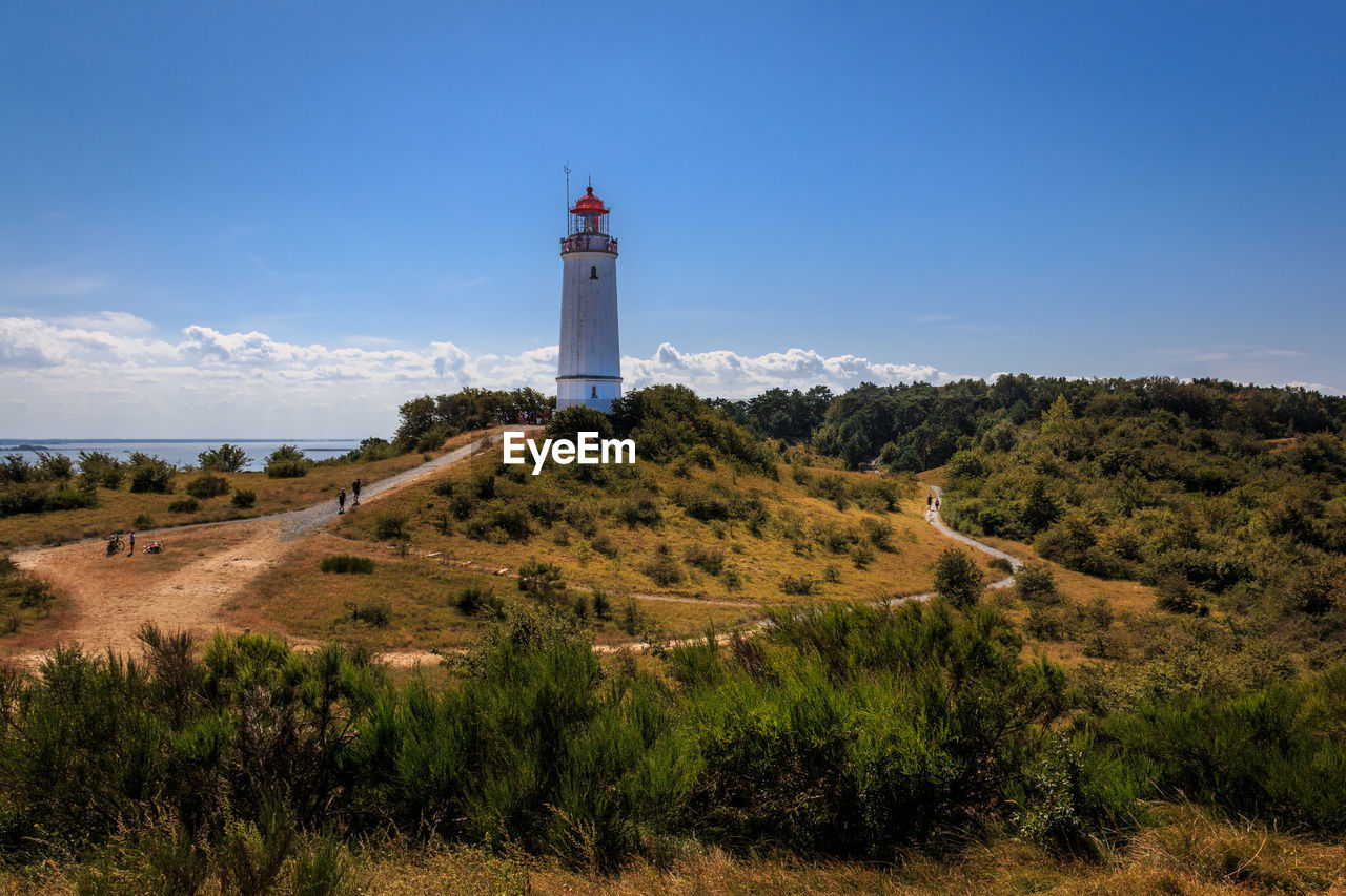 LIGHTHOUSE AMIDST TREES AND BUILDINGS AGAINST SKY