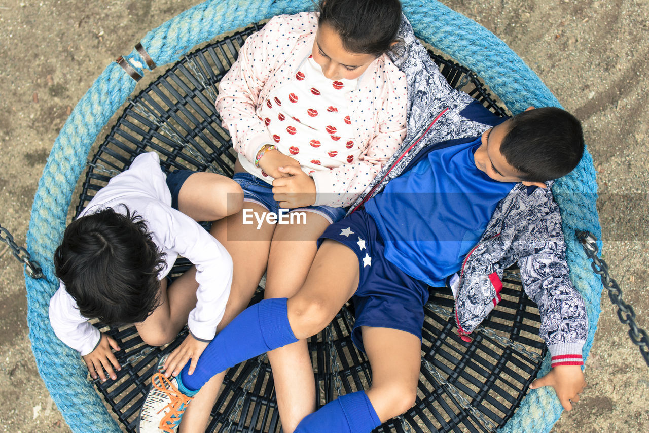 High angle view of siblings sitting on swing at playground