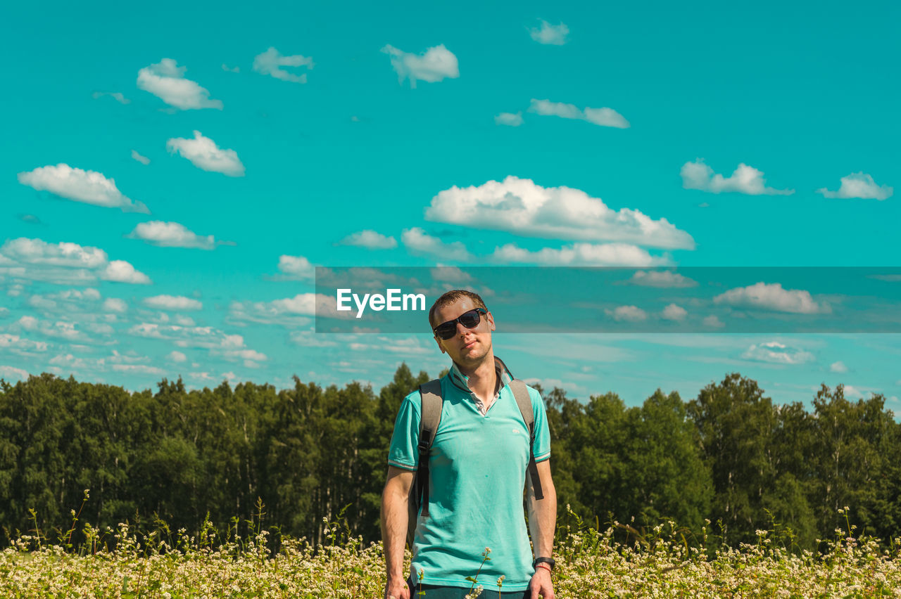 Portrait of young man standing on field against sky