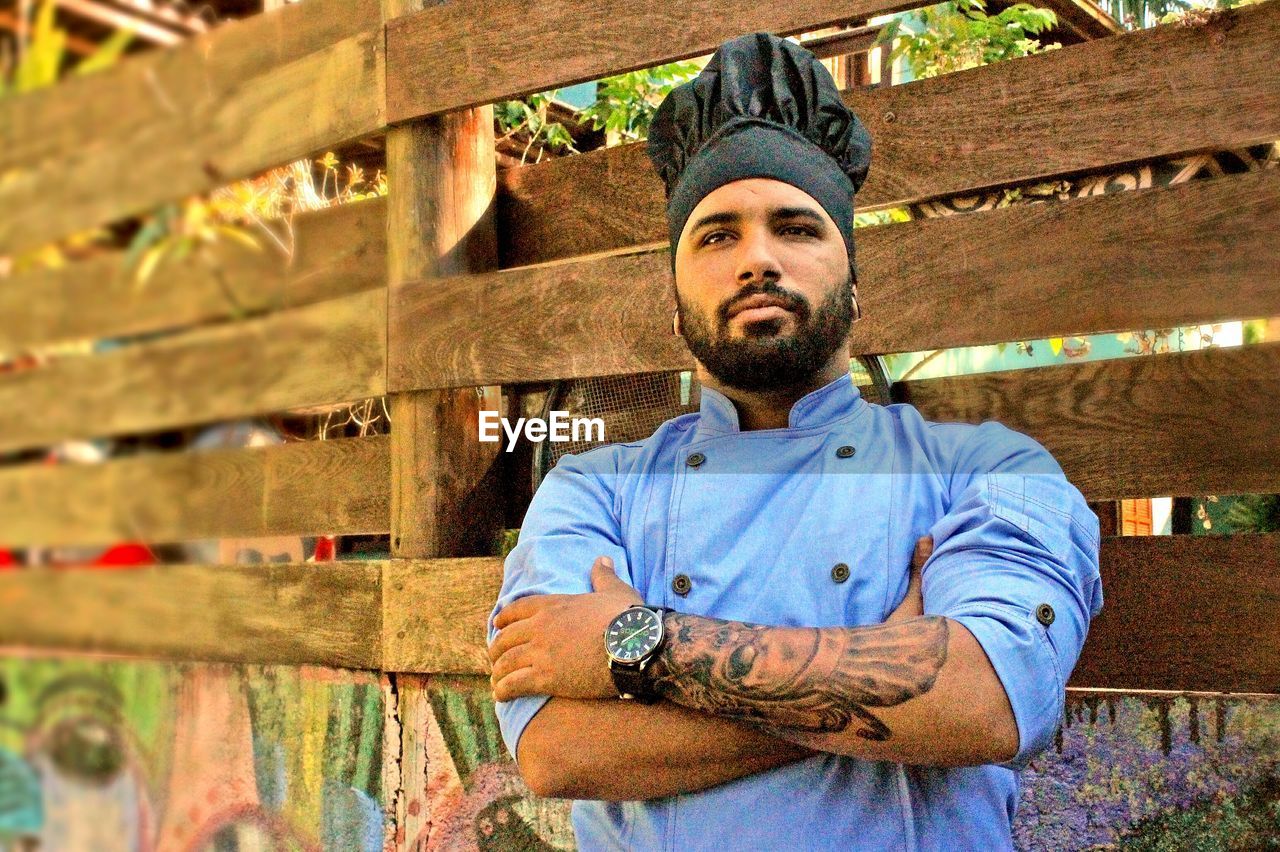 Chef with arms crossed standing by wooden fence