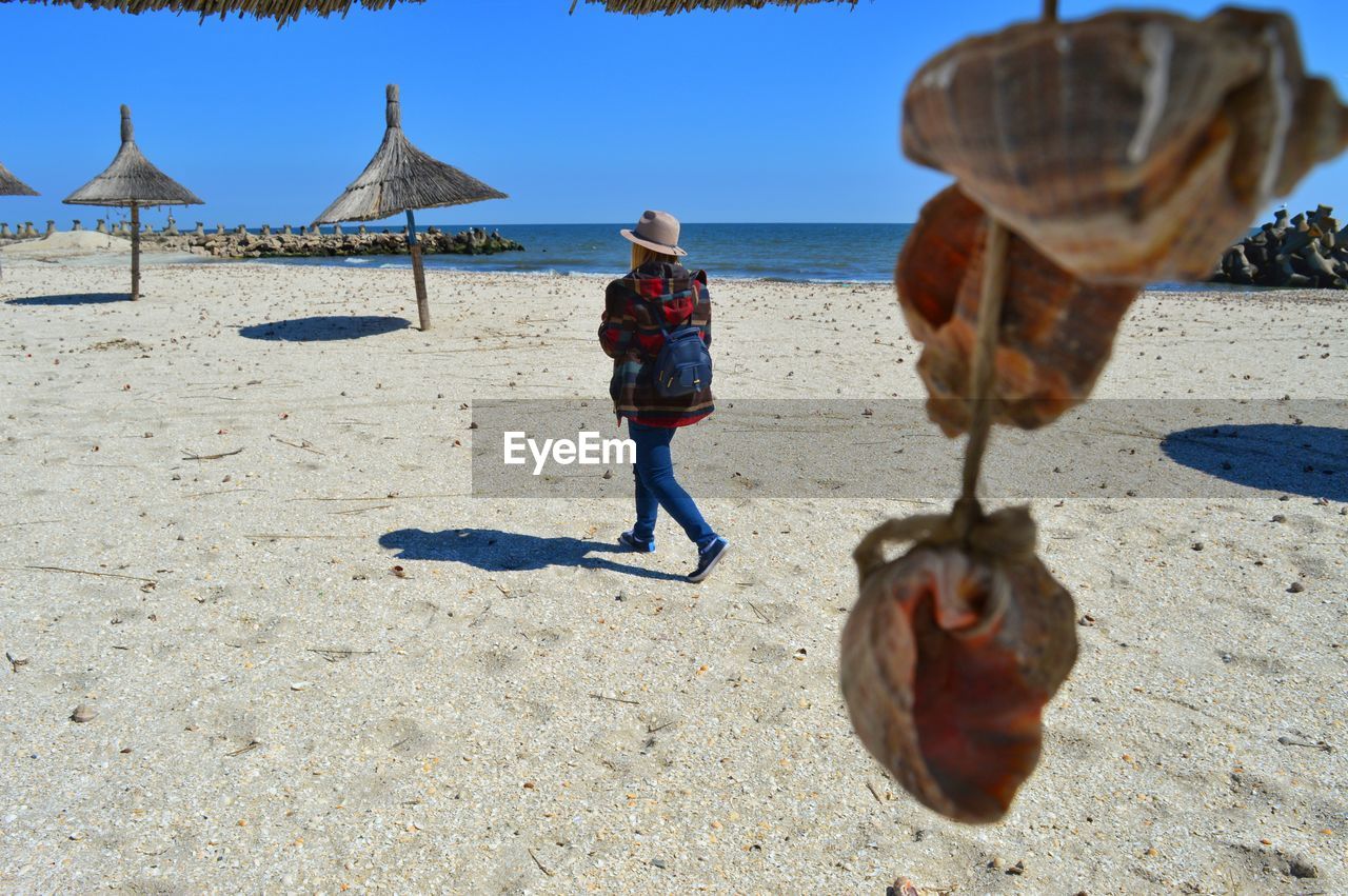 REAR VIEW OF MAN WALKING ON BEACH