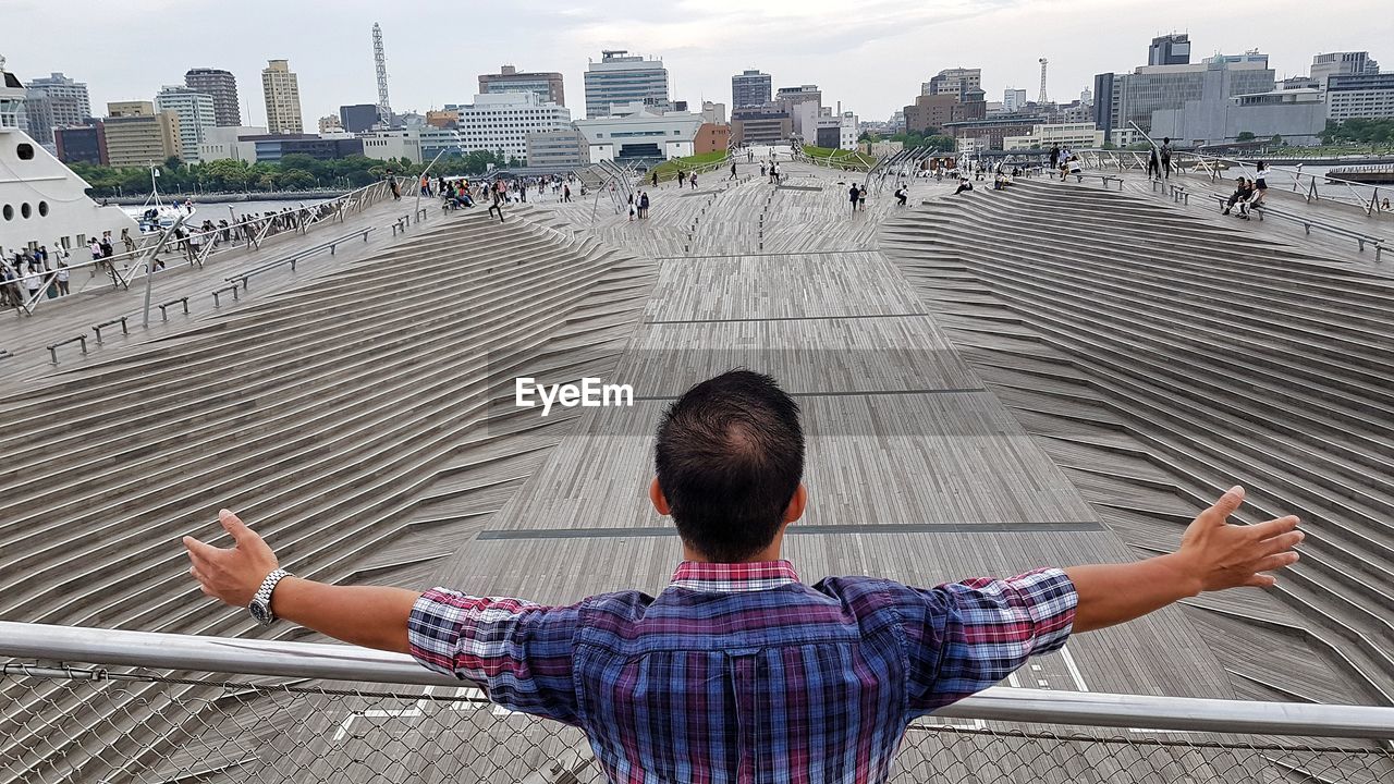 Rear view of man with arms outstretched against buildings in city