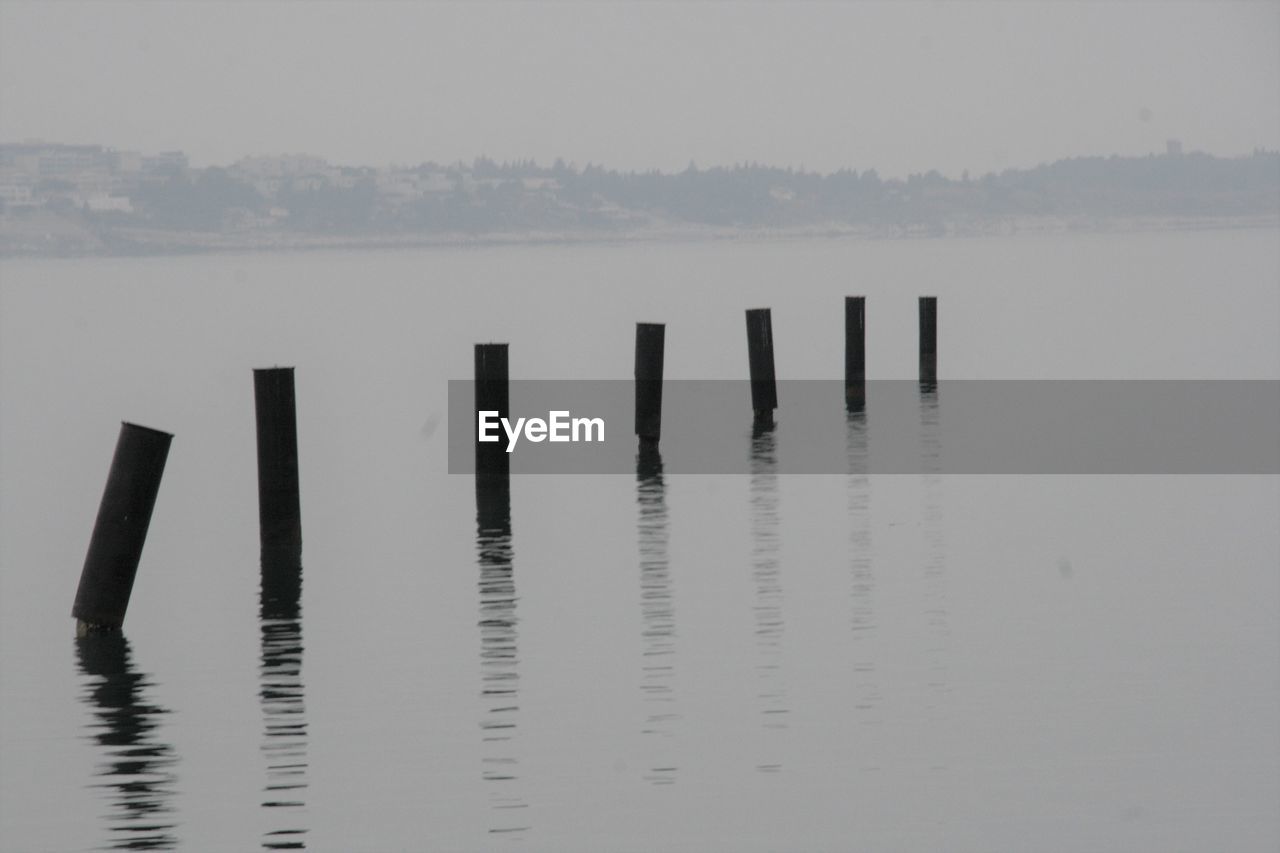 Wooden posts in lake against sky