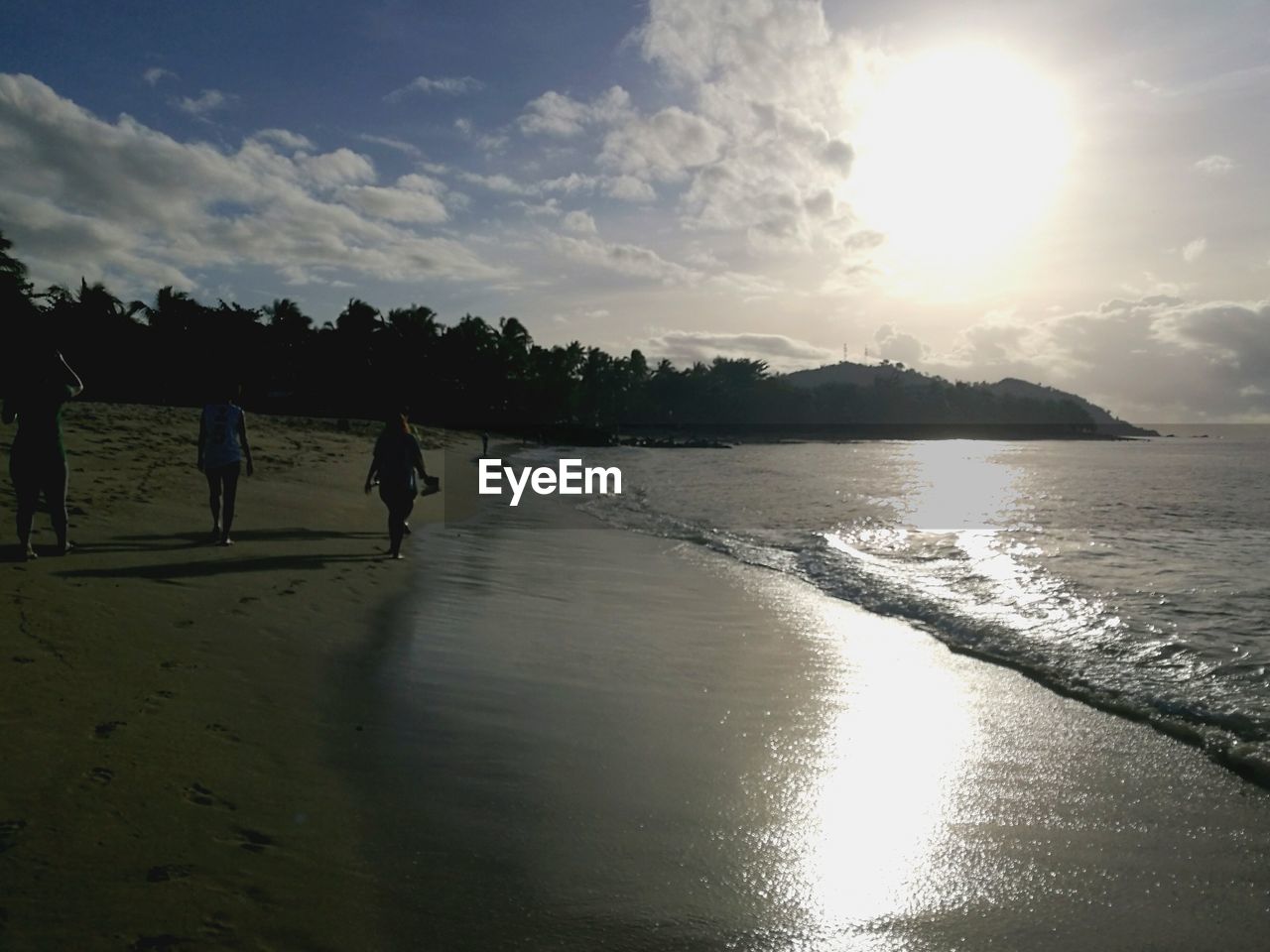 REAR VIEW OF PEOPLE WALKING AT BEACH DURING SUNSET