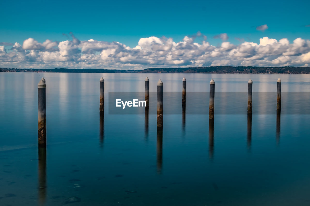 WOODEN POSTS IN SEA AGAINST CLOUDY SKY