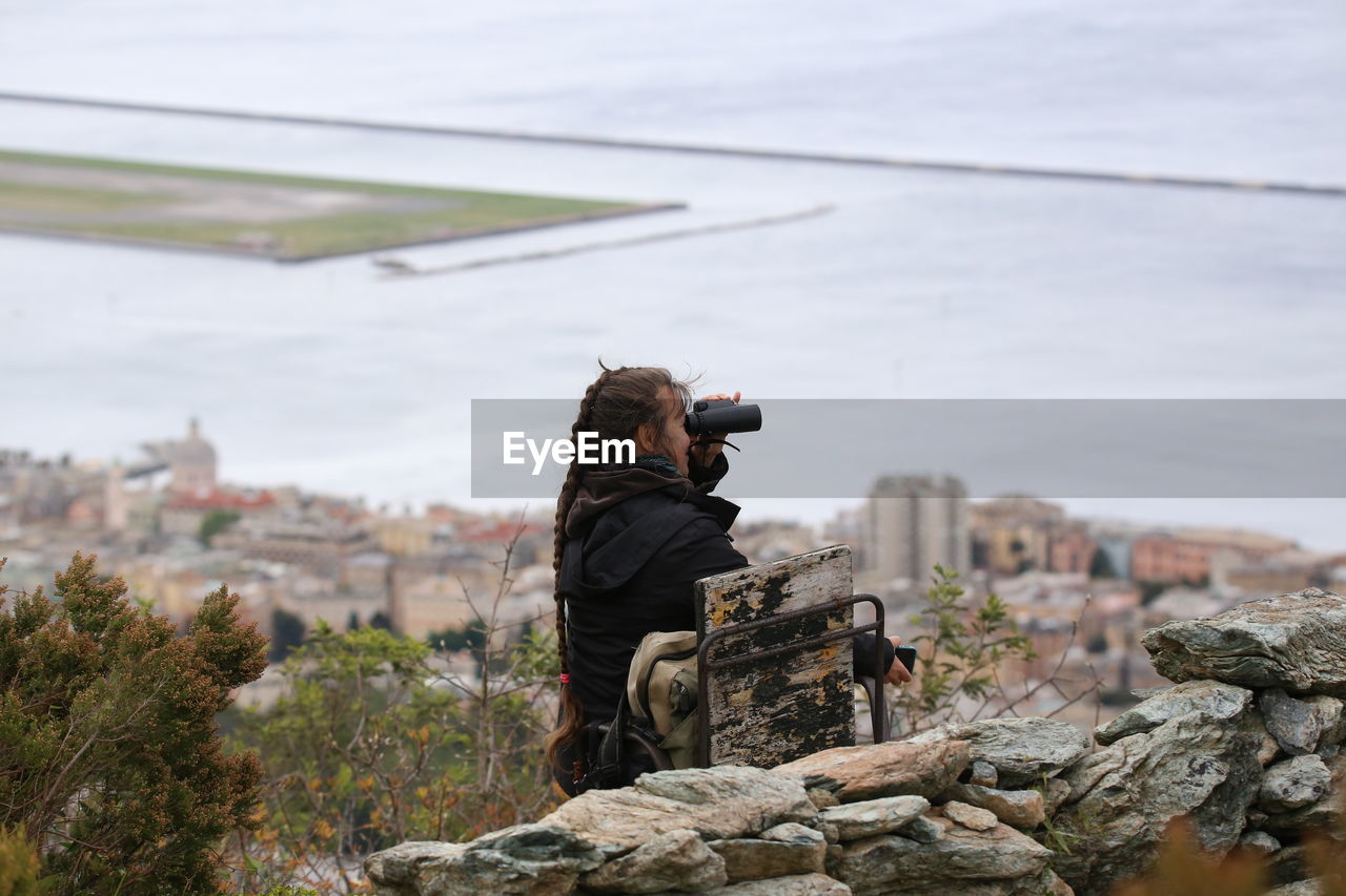 Woman looking through binoculars against sea